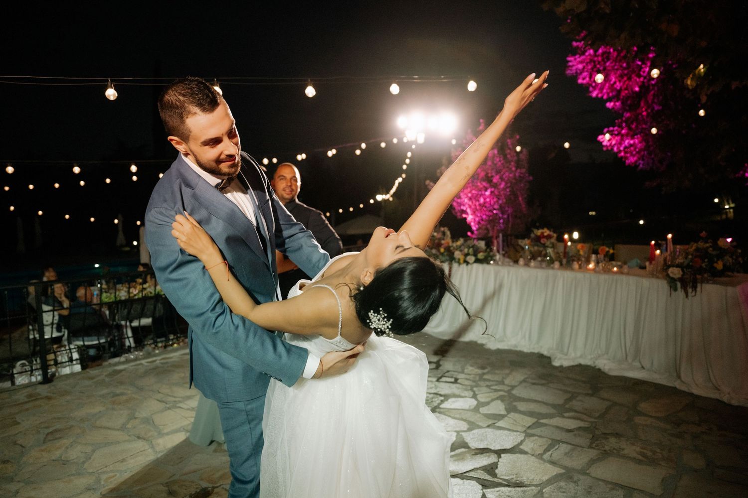 Couples dance together during a romantic evening reception under string lights and magenta floral decorations.