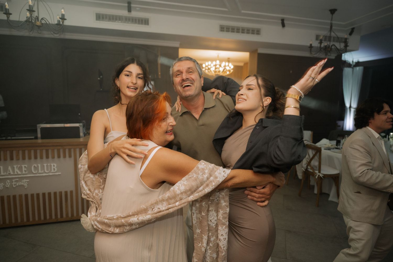 People dancing and celebrating at a wedding reception in an indoor venue with dim lighting.