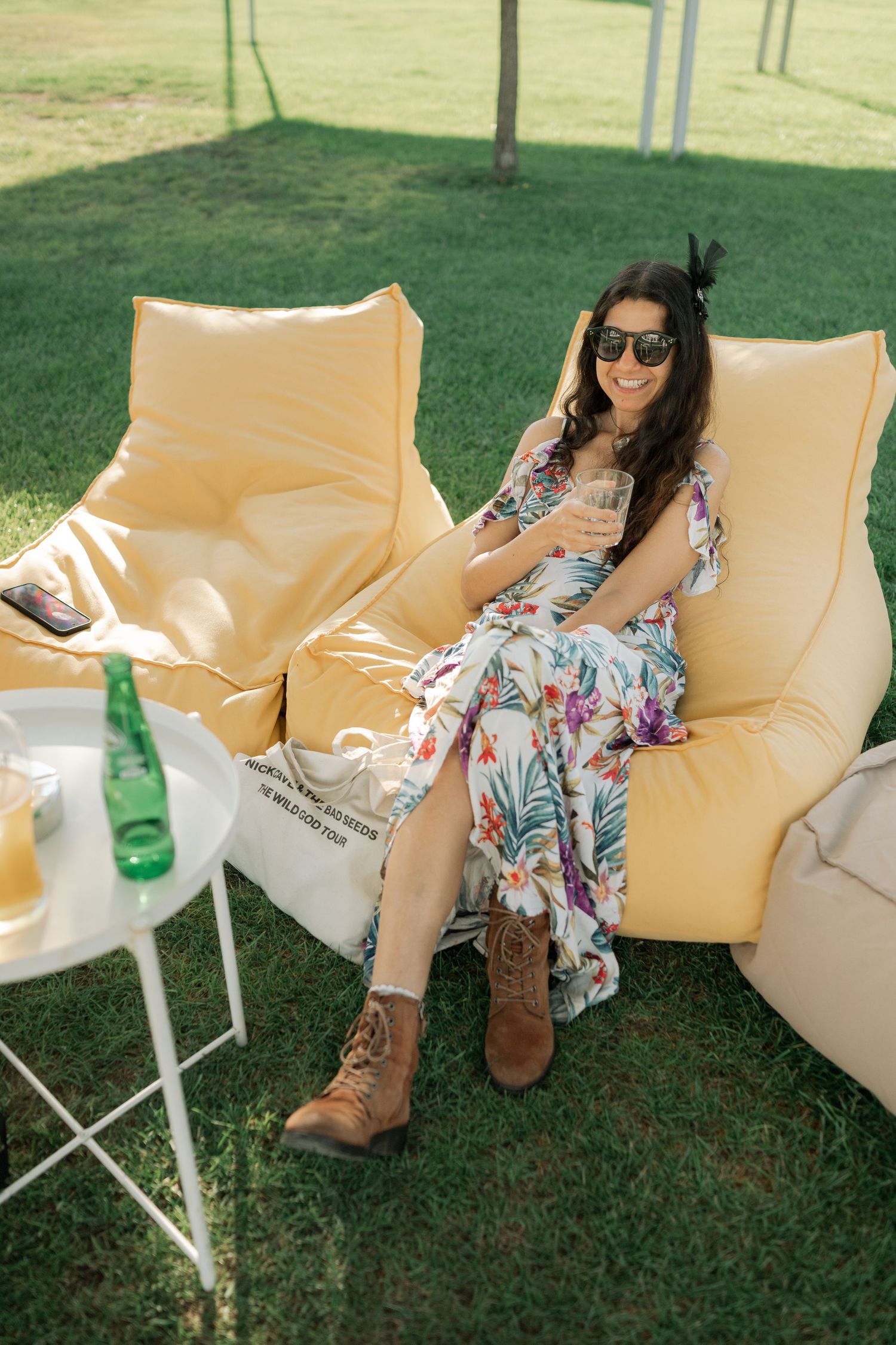 Person relaxing on cream-colored outdoor furniture on green lawn with brown boots and floral dress.