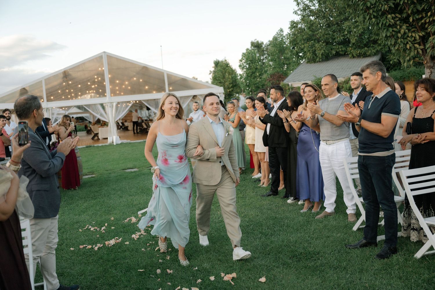 Wedding guests line up outdoors to watch a couple dancing at a garden reception celebration.