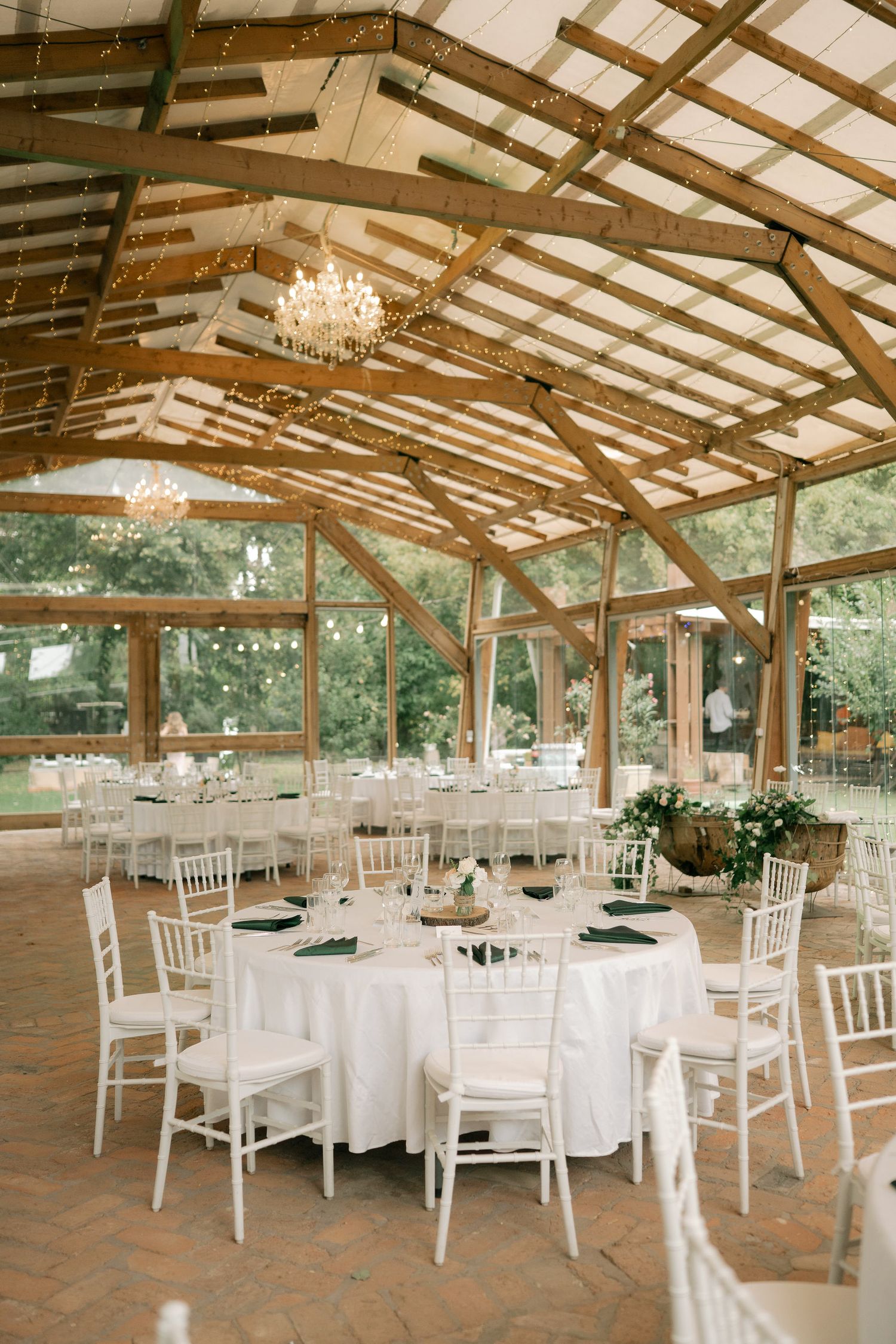 Rustic wooden pavilion decorated with white tables, chairs, and chandeliers for an elegant outdoor wedding reception.