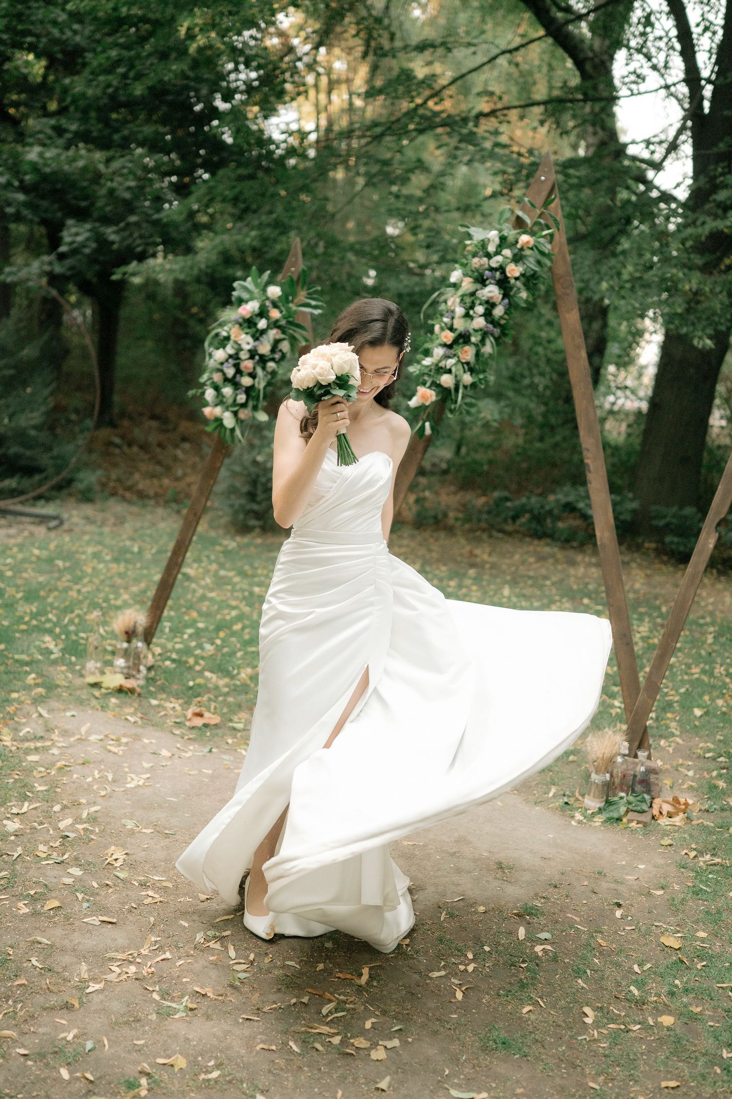 A person in a flowing white wedding dress twirls playfully in a wooded outdoor setting during a photo session.