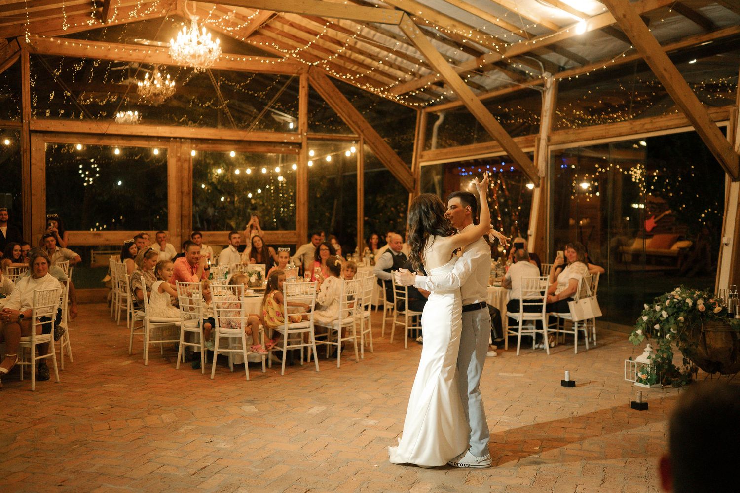 A couple shares their first dance in a rustic barn venue decorated with chandeliers and string lights for their wedding reception.