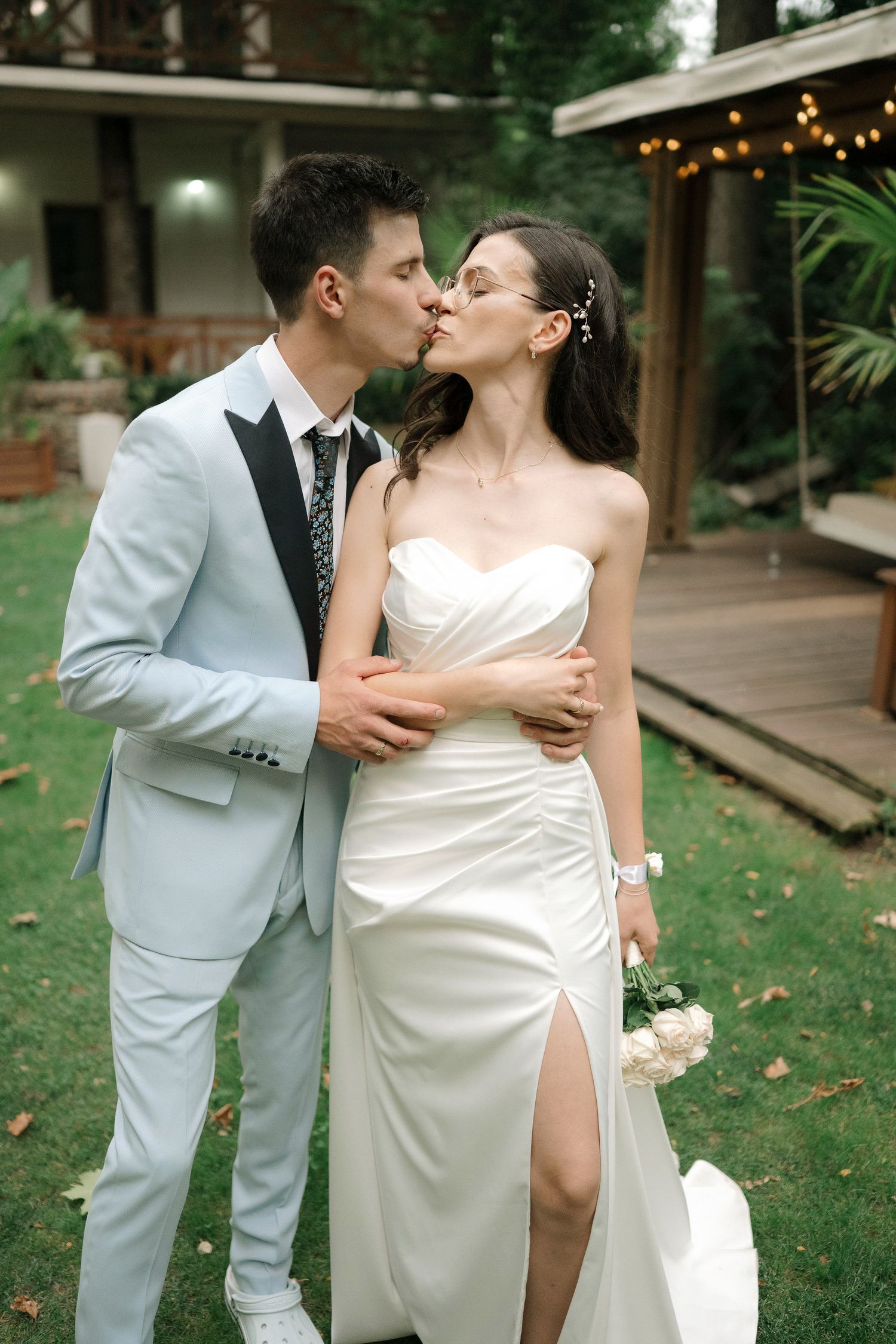 Romantic wedding couple shares intimate moments in an outdoor garden setting with string lights and greenery.
