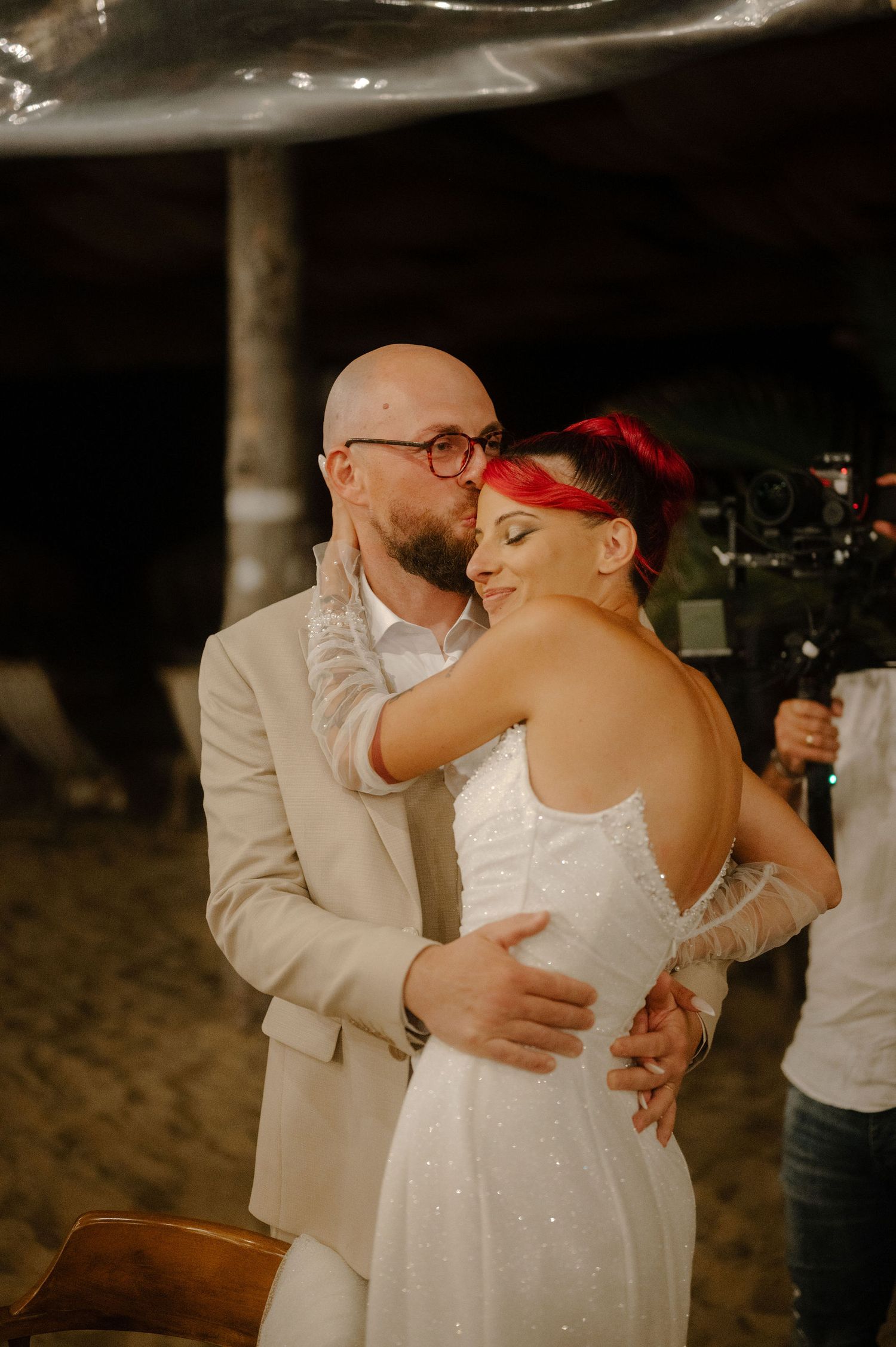 A couple shares a romantic dance at an evening wedding reception on a beach.