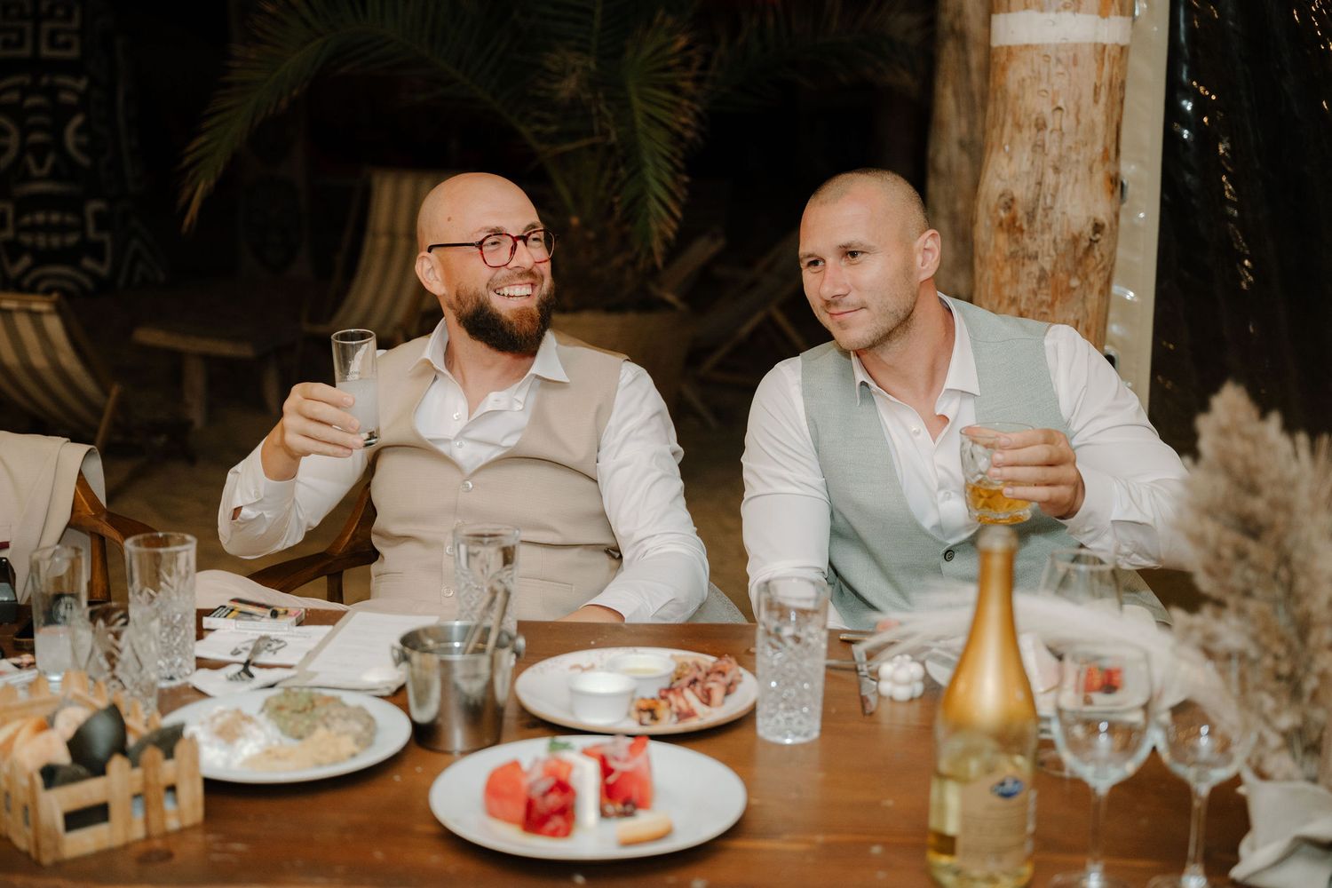 Wedding guests enjoy a candlelit dinner reception at a rustic venue with elegant table settings and glowing ambiance.