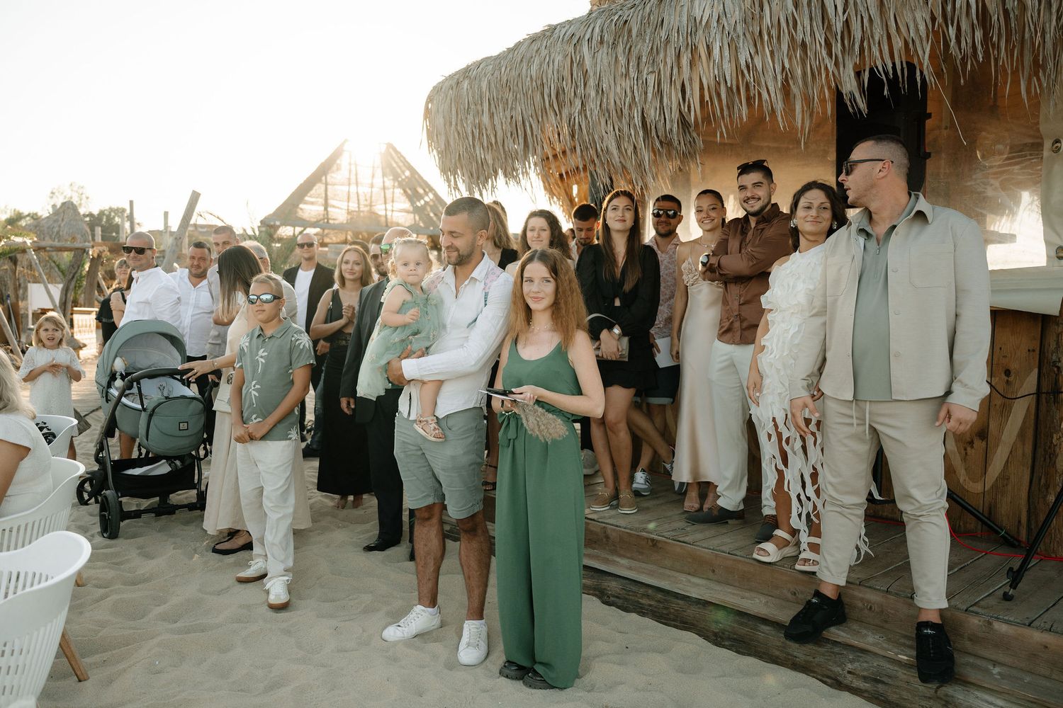 Wedding guests in light colored attire gather along a rustic outdoor pathway during a summer celebration.