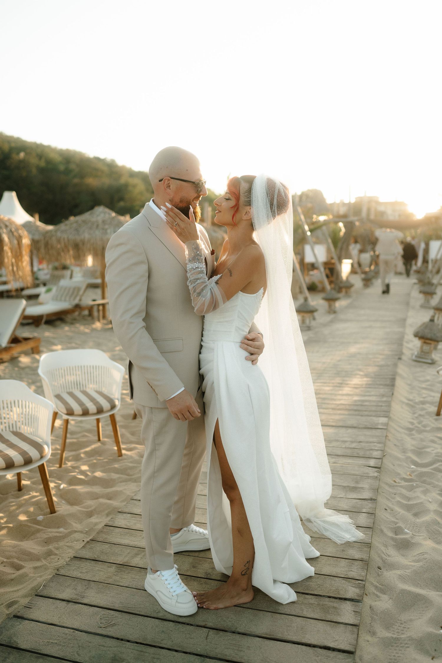 Newlywed couple shares intimate moments on a wooden boardwalk at sunset during their beach wedding photoshoot.