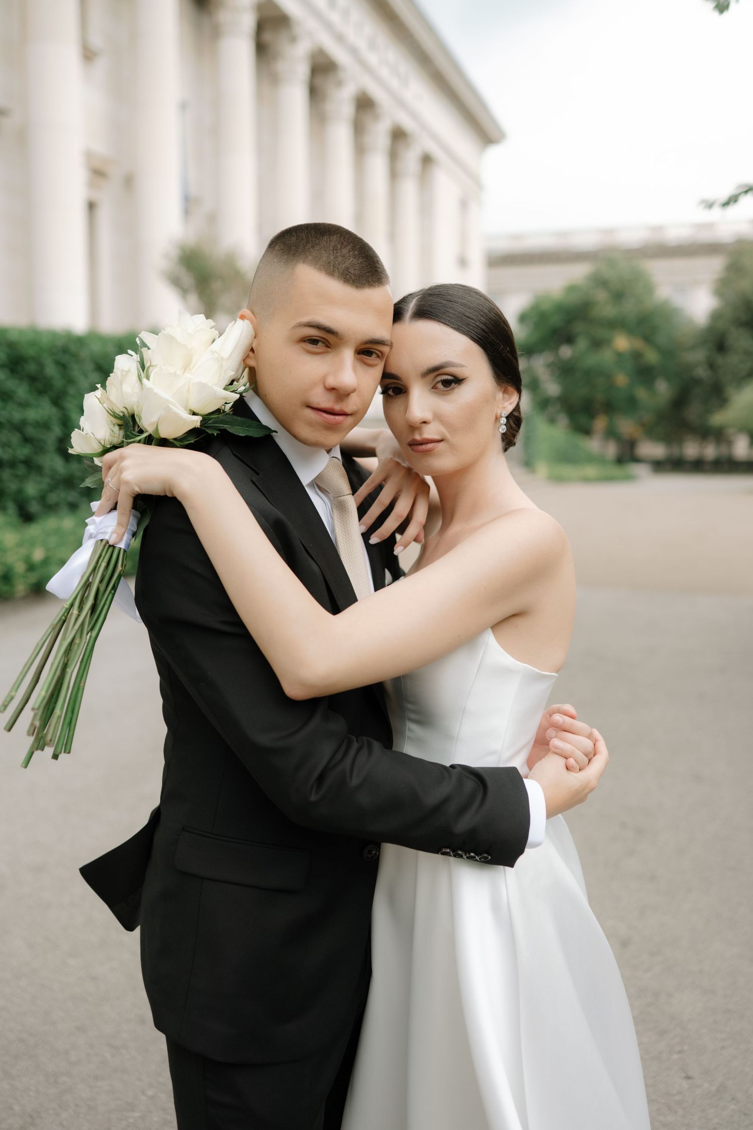 A romantic wedding couple embraces while dancing outdoors near elegant white columns.