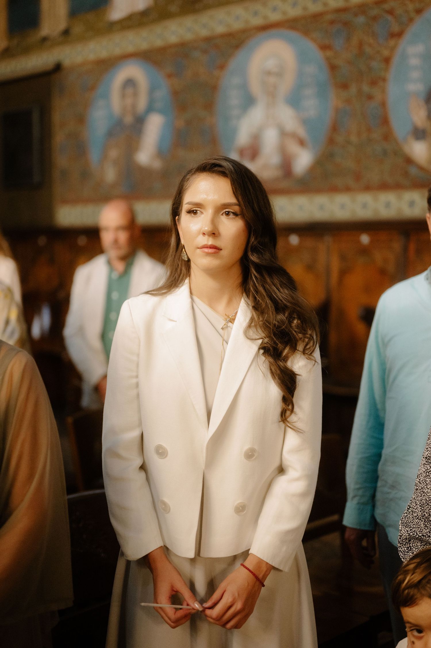 Person in white blazer standing in an ornate church interior with religious icons and murals visible in background.
