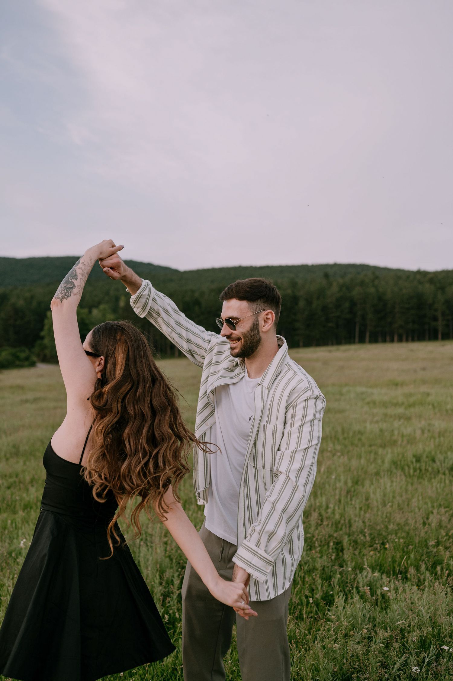 A couple in a green meadow dancing together, with the woman wearing black and the man in a striped shirt.