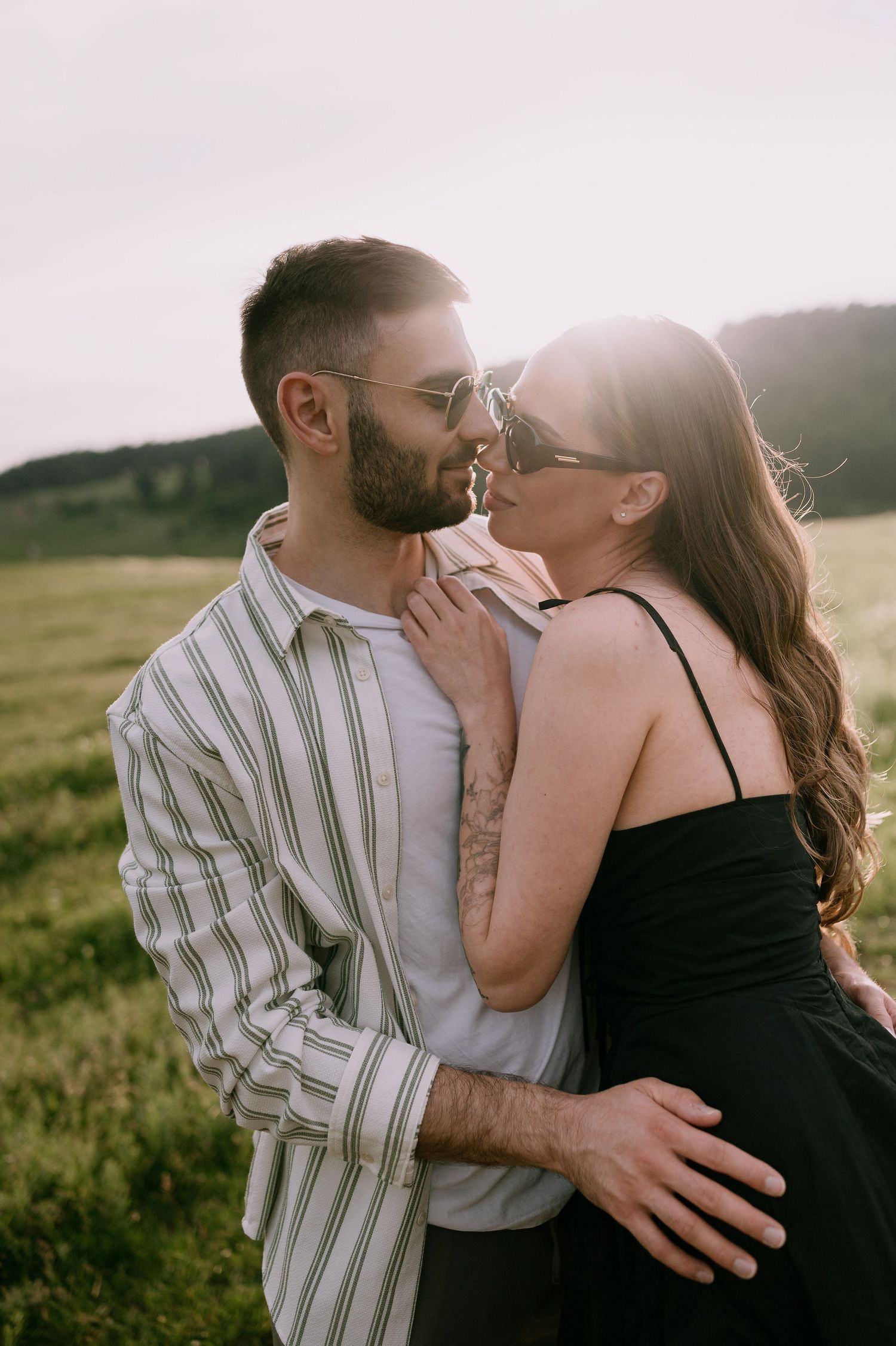 A tender moment between a couple sharing an intimate embrace against a natural outdoor backdrop at sunset.