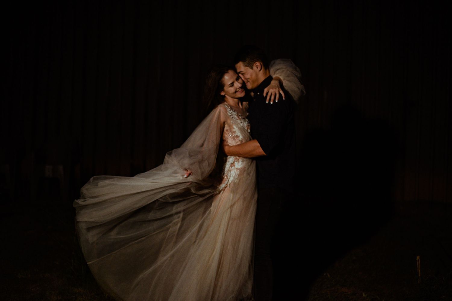 A romantic couple in elegant wedding attire dances and embraces in a series of dramatic black and white photographs.