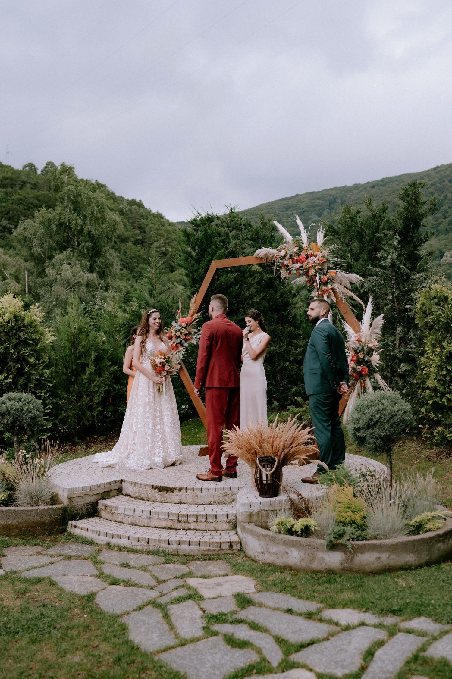 Outdoor wedding ceremony with guests gathered on stone platform surrounded by mountains and greenery.
