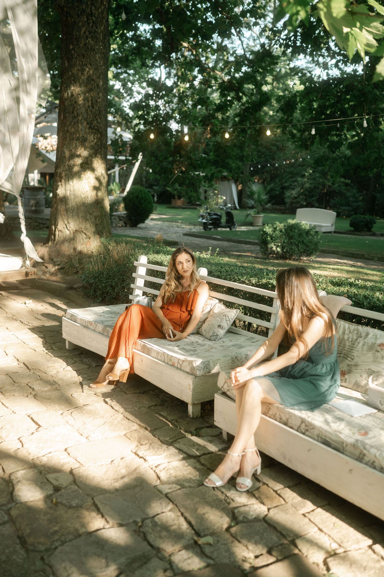 A person in casual attire relaxes on a white wooden bench in a sunlit garden setting.