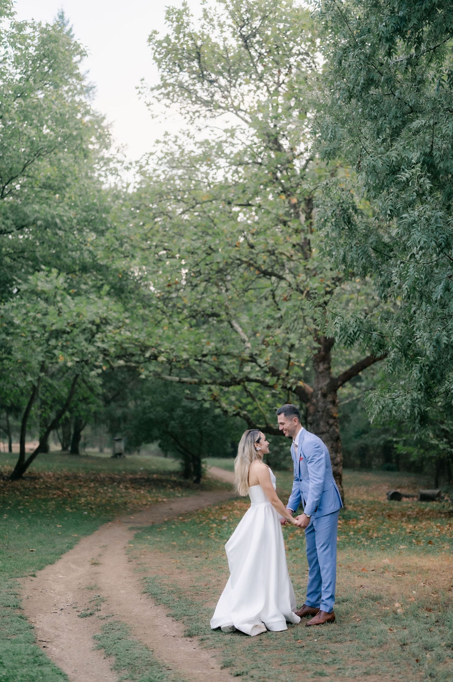 A couple shares a romantic moment in a blooming orchard with winding dirt paths and lush greenery.