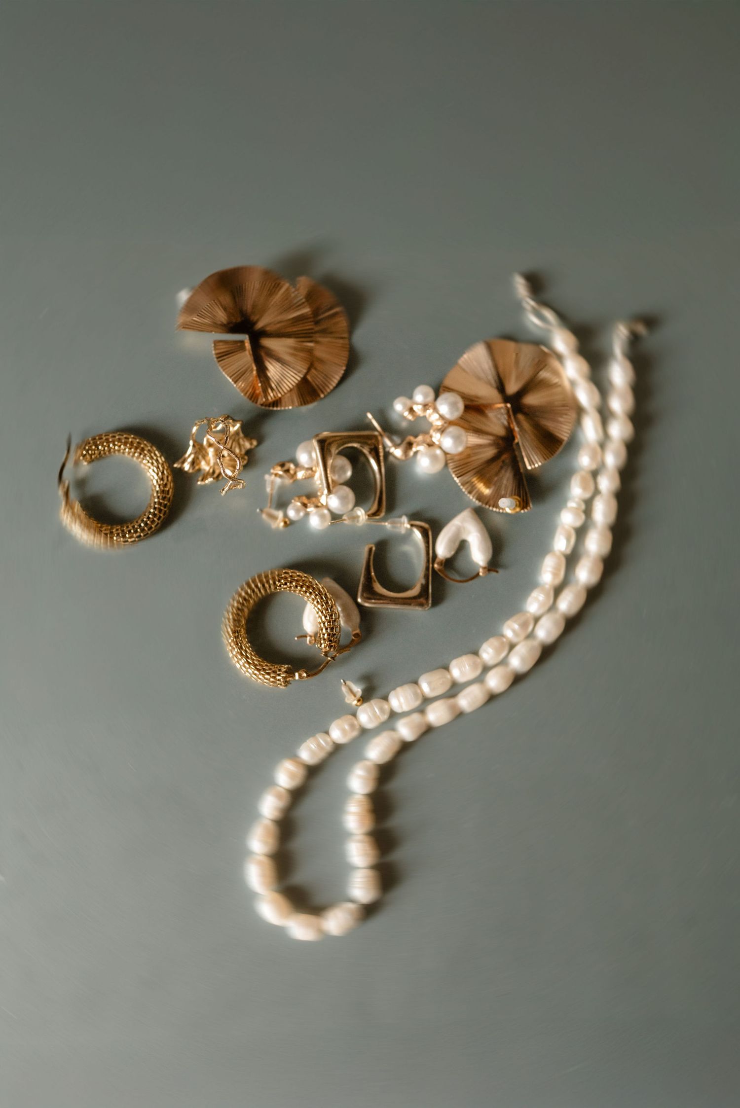A collection of gold earrings and a pearl necklace arranged artistically on a gray background.