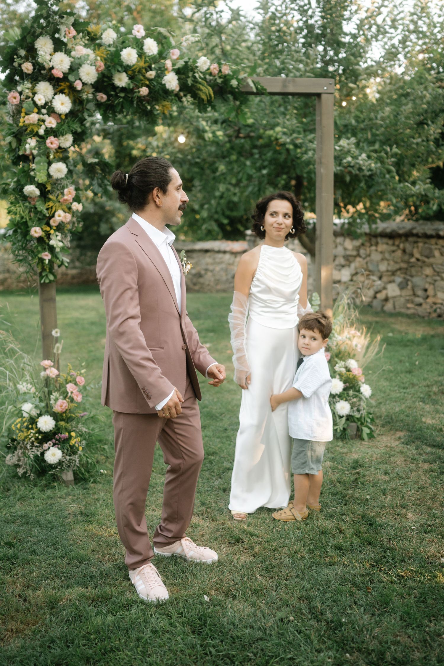 Family in coordinated outfits poses together in a garden setting with blooming white roses and greenery.
