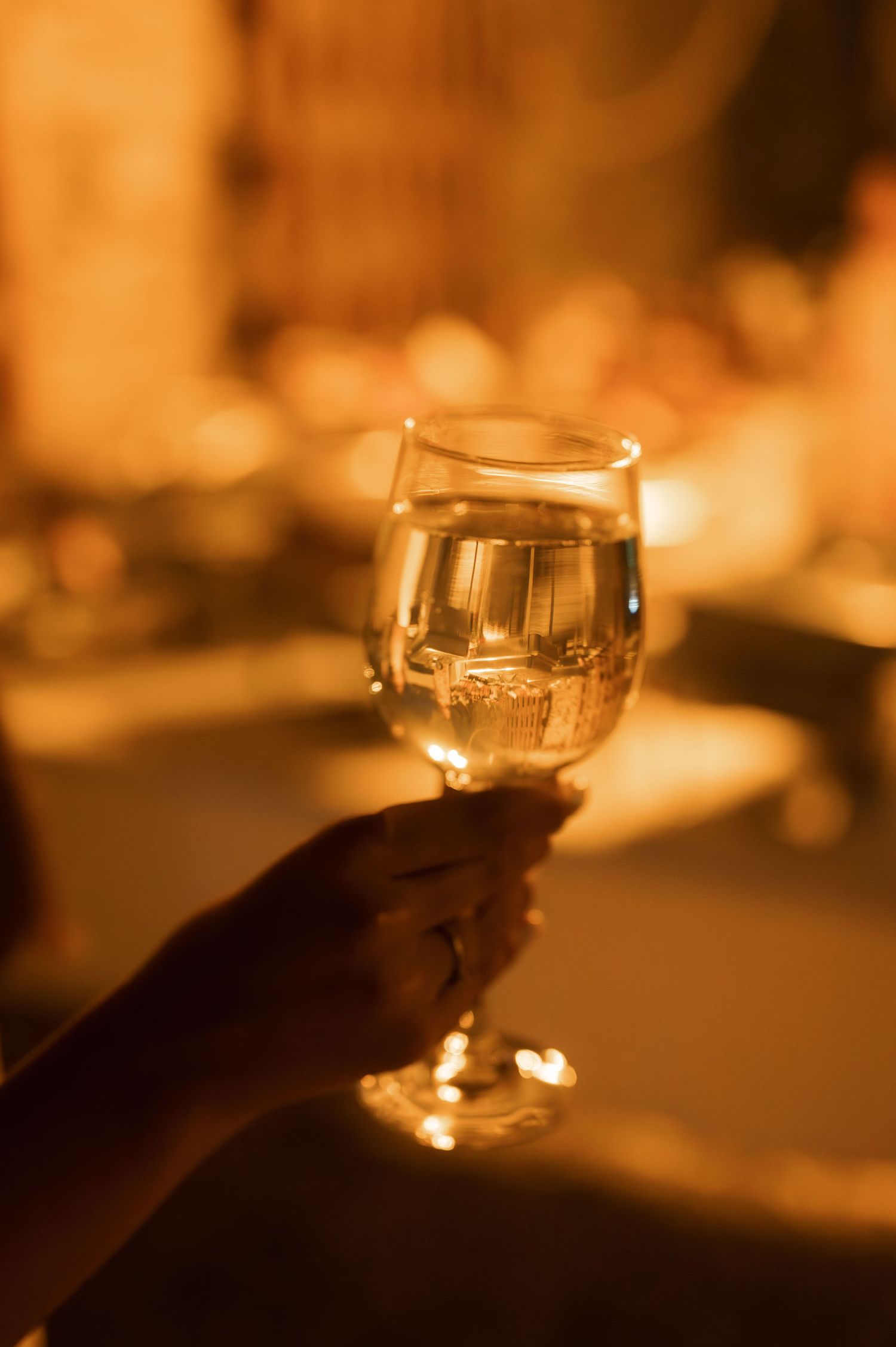 A glass of white wine illuminated by warm candlelight creates an intimate atmosphere in a dimly lit setting.