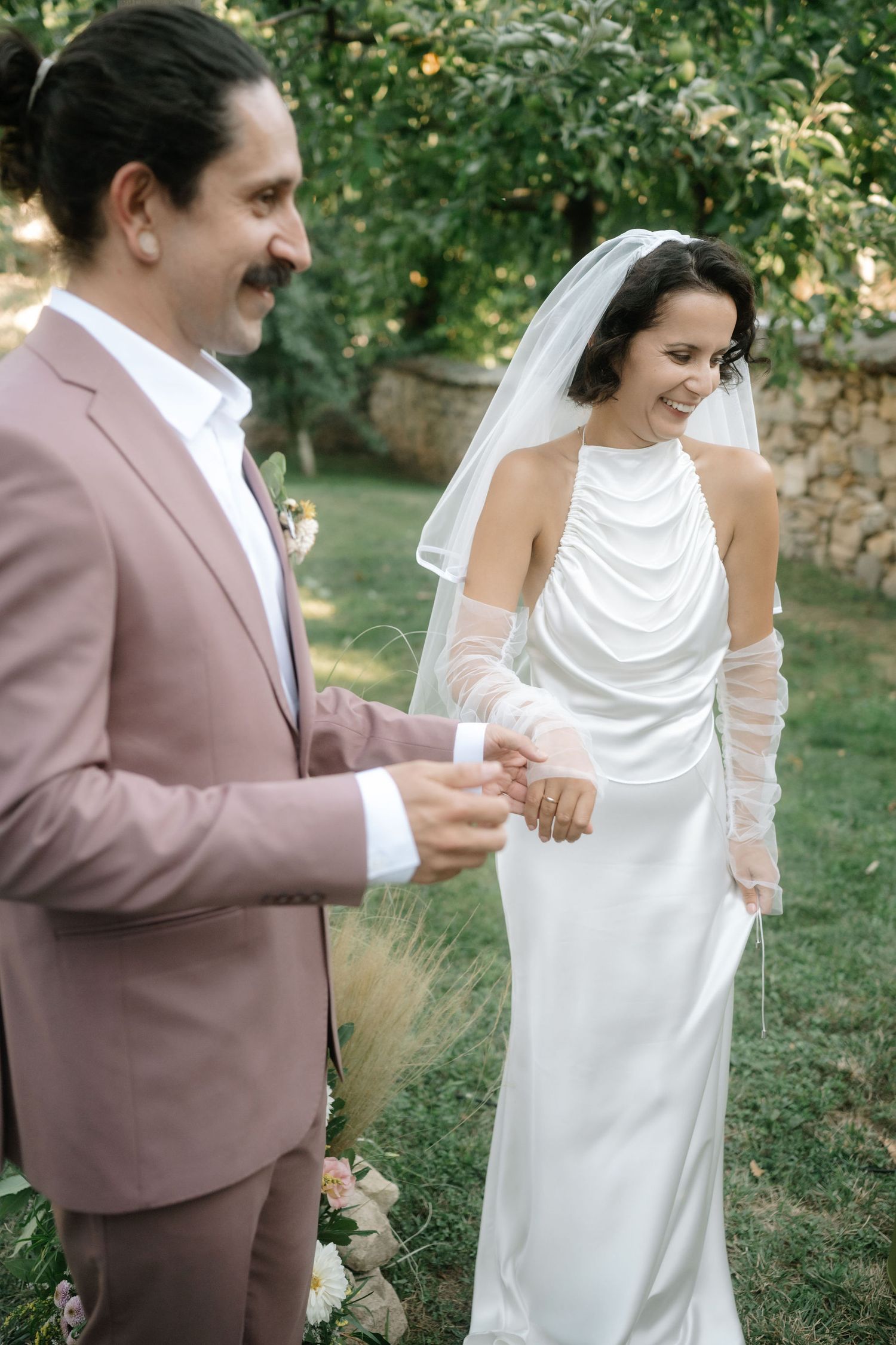 A couple shares a tender moment dancing together in a garden setting while wearing wedding attire.