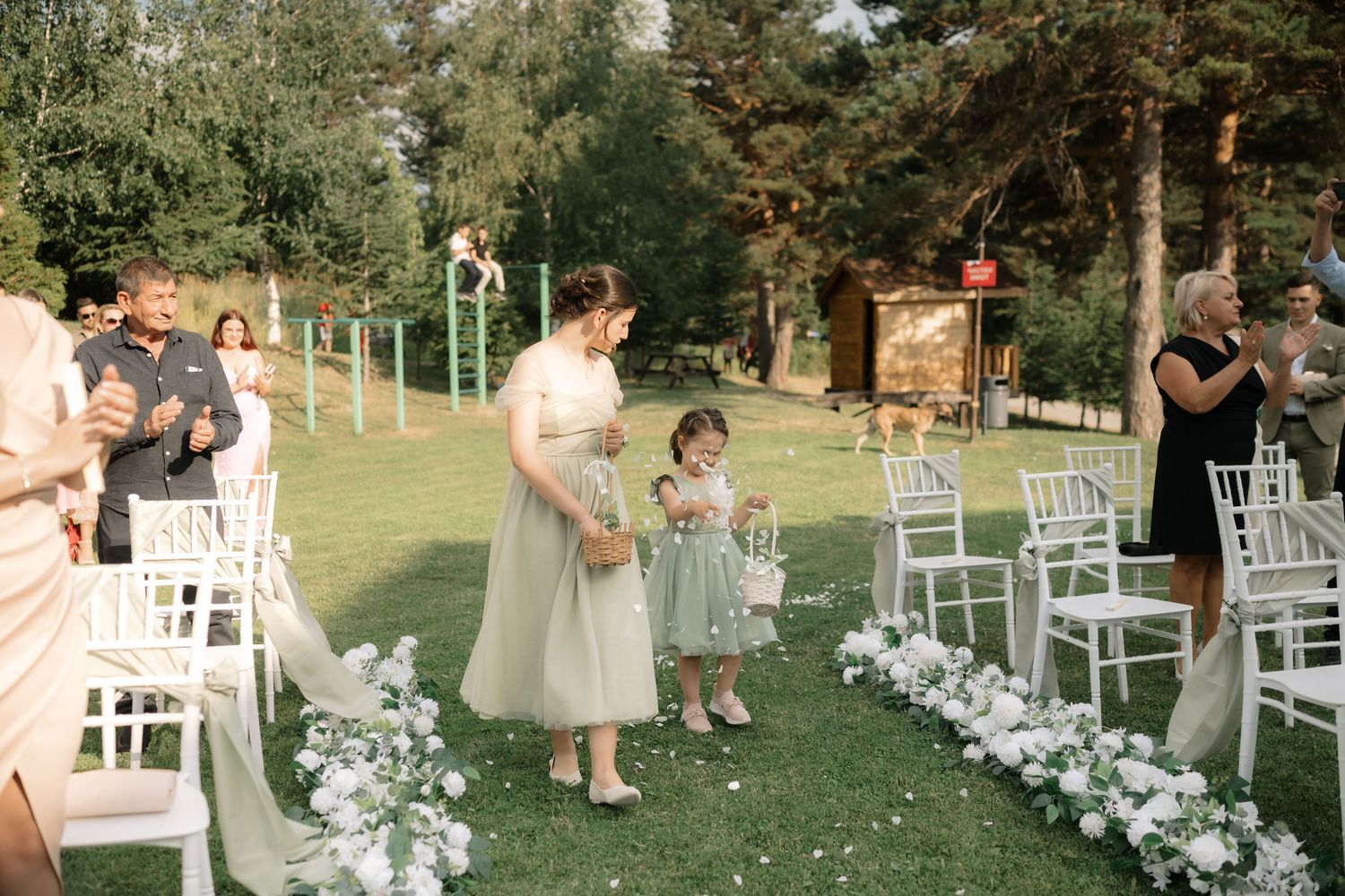 Wedding ceremony setup in a garden with white chairs and floral arrangements along the aisle.