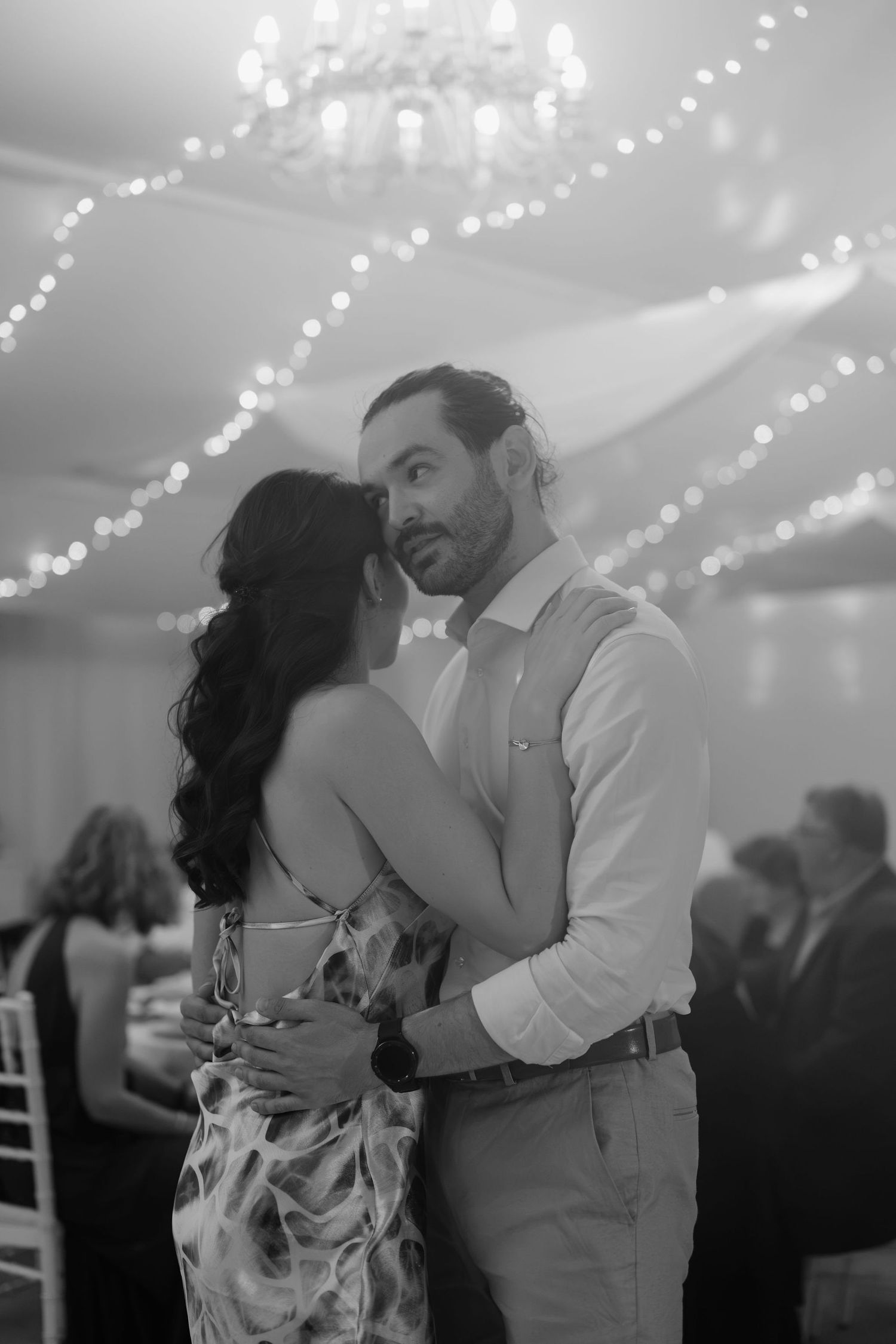 Black and white photo of a couple sharing an intimate dance at an elegant event venue with twinkling lights overhead.