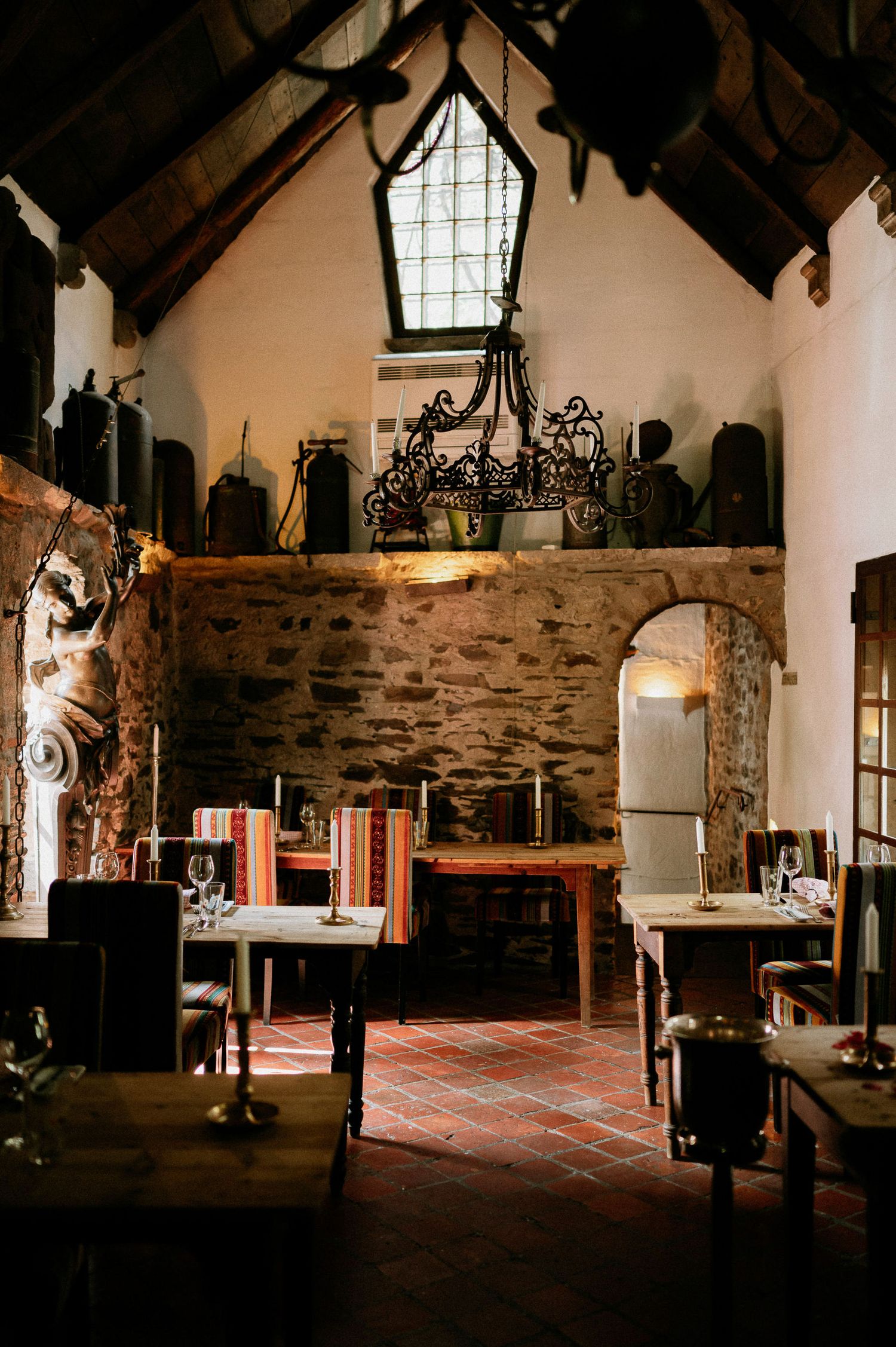 Interior view of a rustic stone hall with vaulted wooden ceiling and natural lighting.