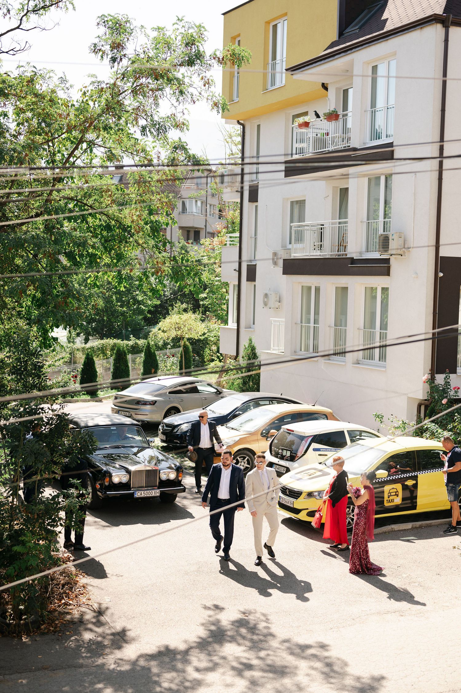 Wedding party walking outside a yellow building with parked cars in the background.