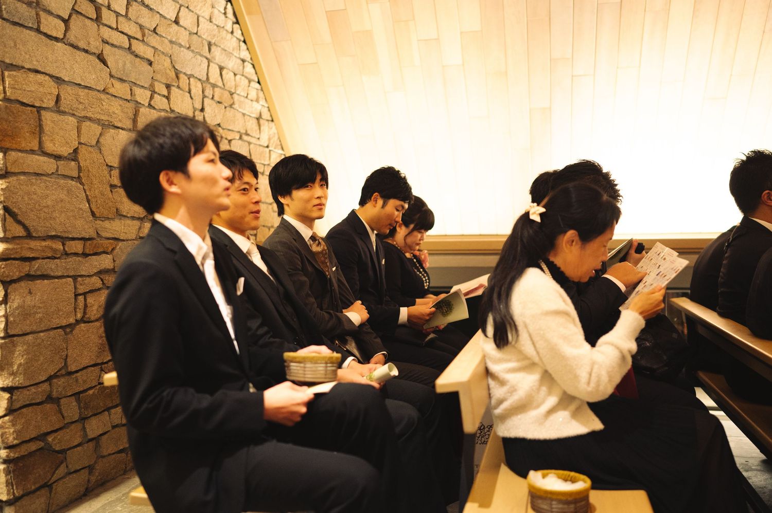 Group seated in formal attire at an event with stone wall and wooden lattice background.