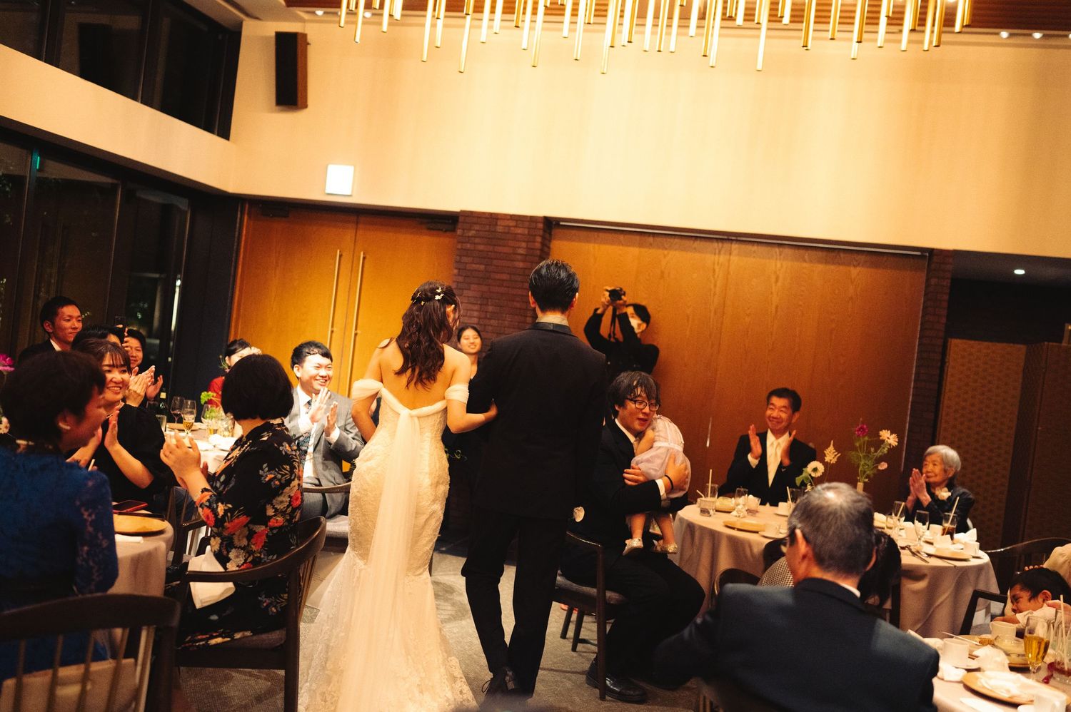 Wedding reception hall with elegant lighting and guests celebrating at tables.
