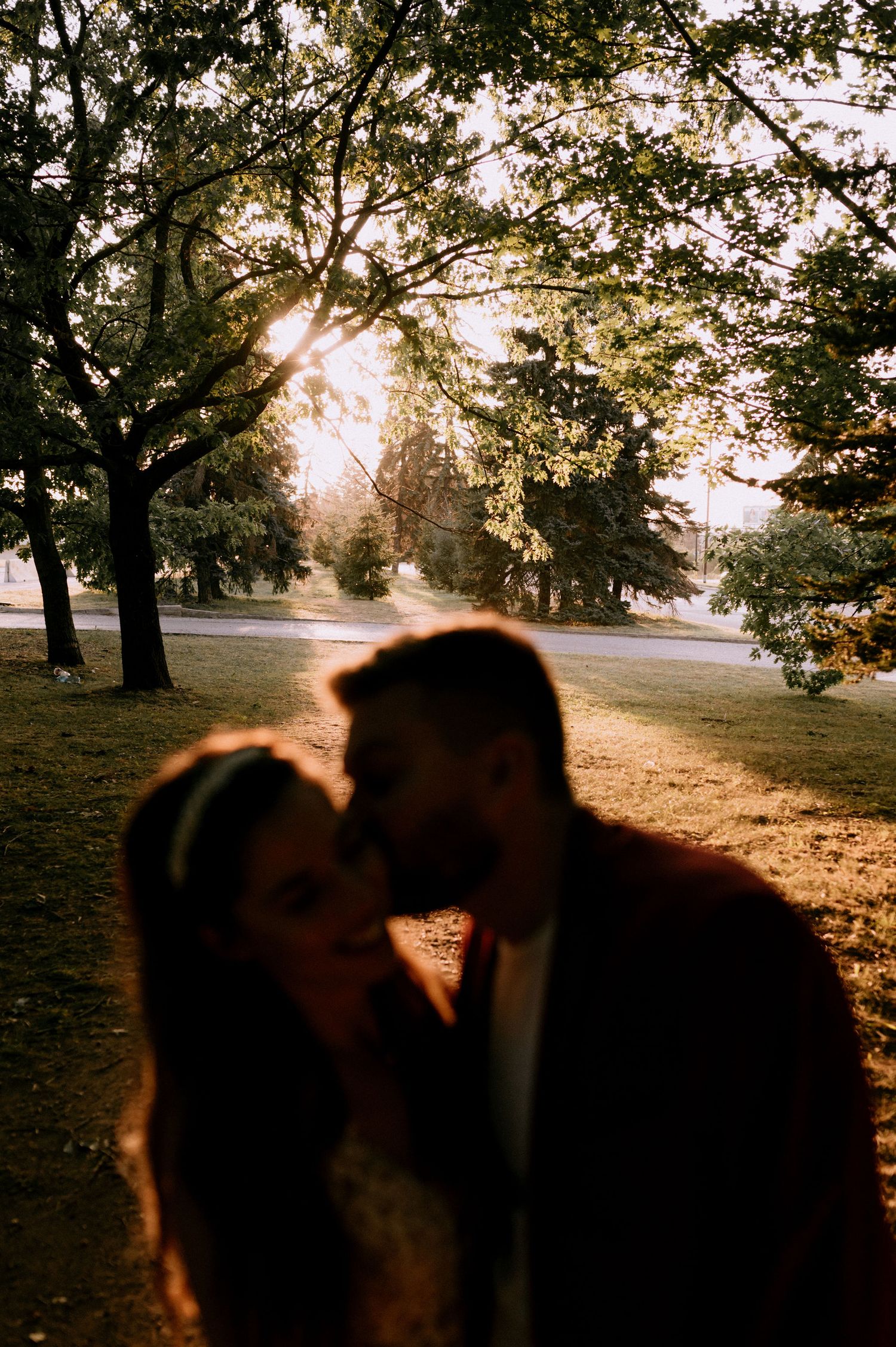 Silhouetted couple shares an intimate moment at sunset in a park setting.