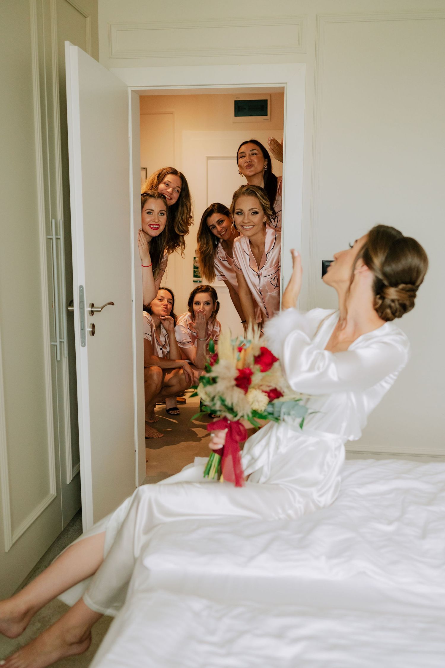 Wedding morning reveal moment with bride on bed and bridesmaids entering room.