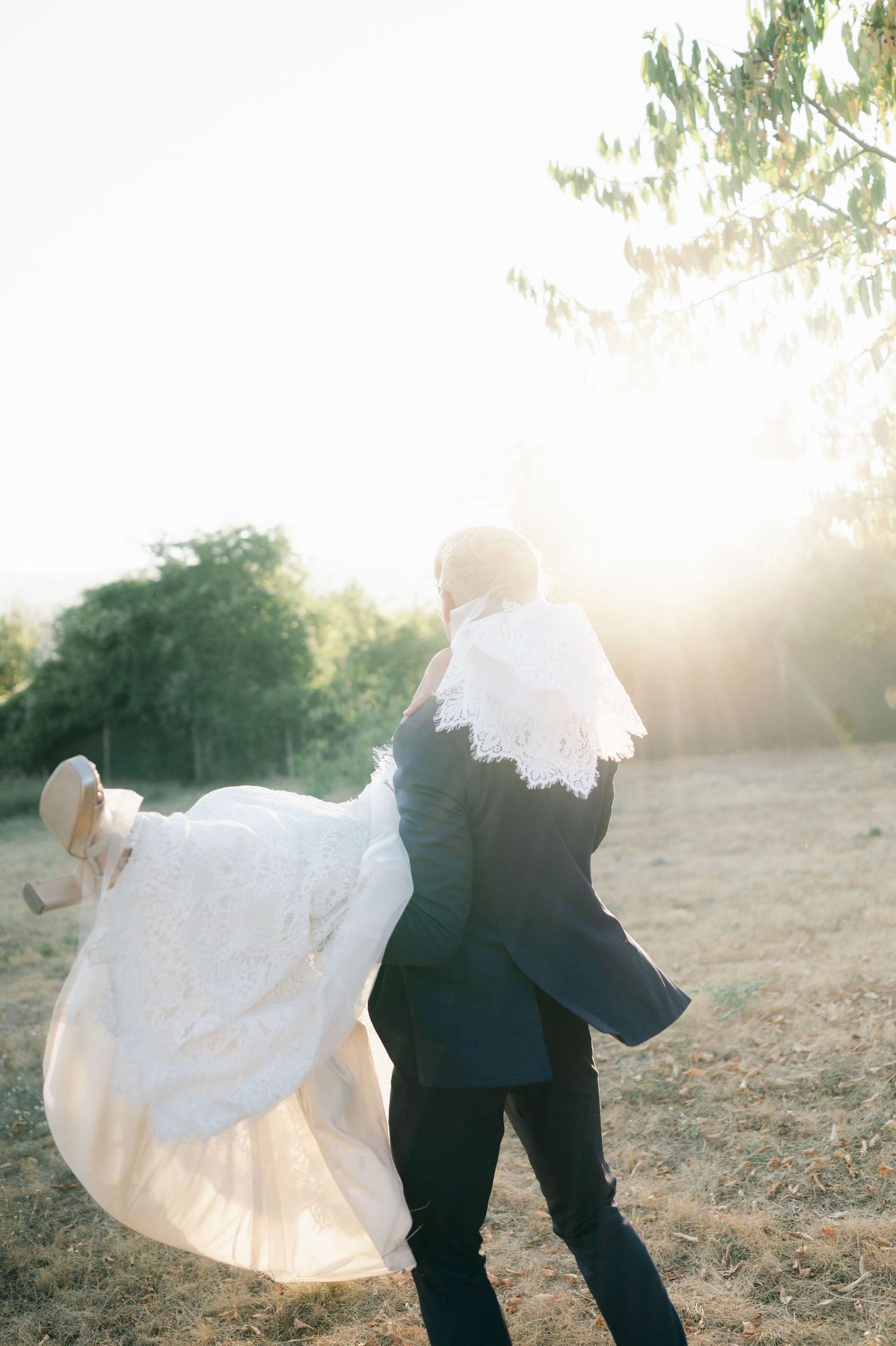 Sunlit silhouettes of newlyweds dancing in a field with bride's dress catching the golden light.