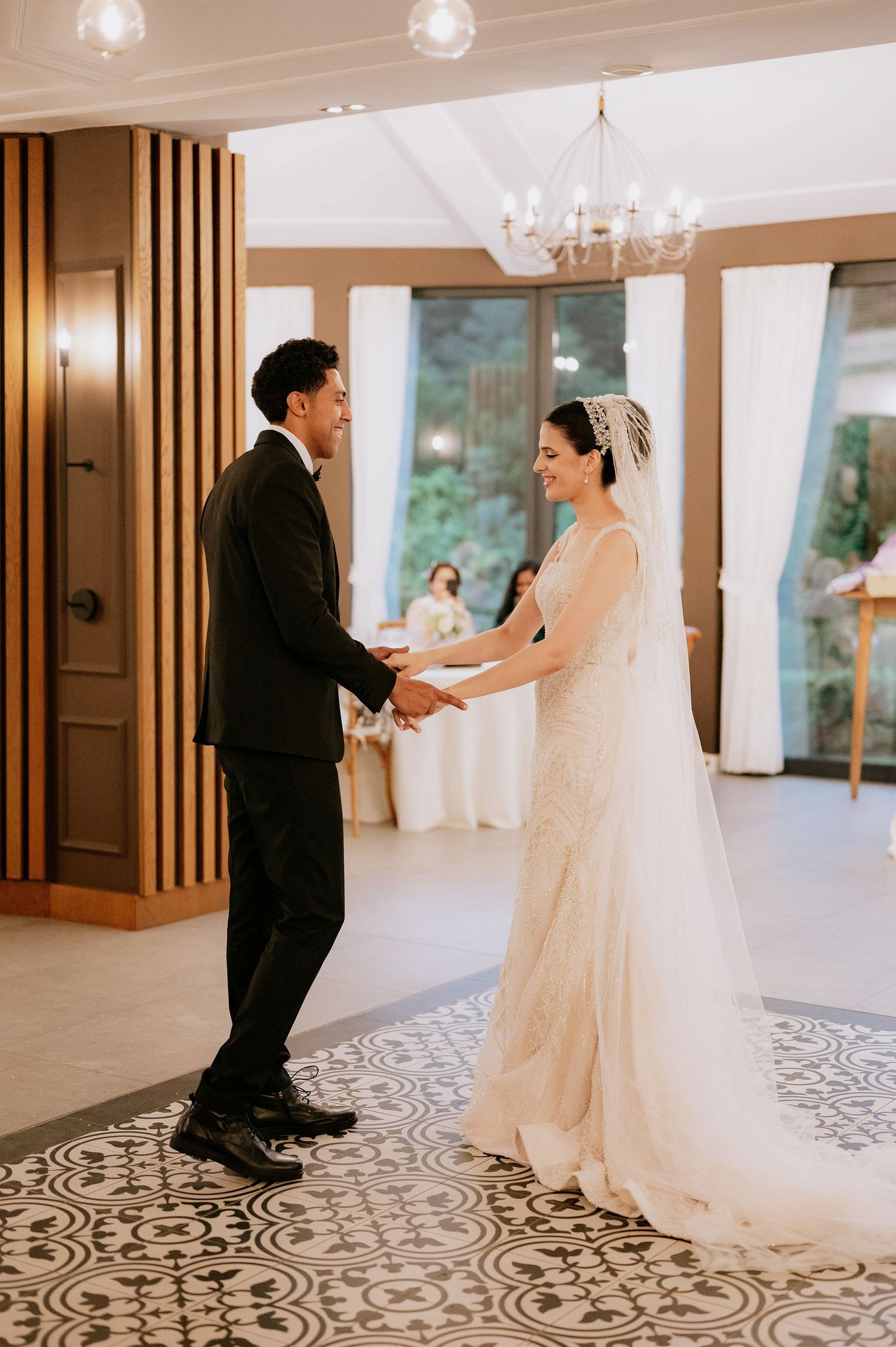 A couple shares their first dance in an elegant ballroom with wooden accents and chandeliers.