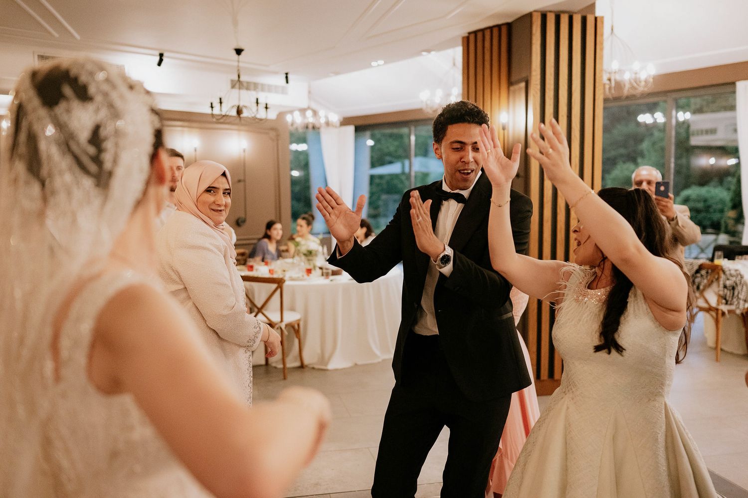 Wedding celebration with guests dancing in a warmly lit reception hall with wooden accent walls.