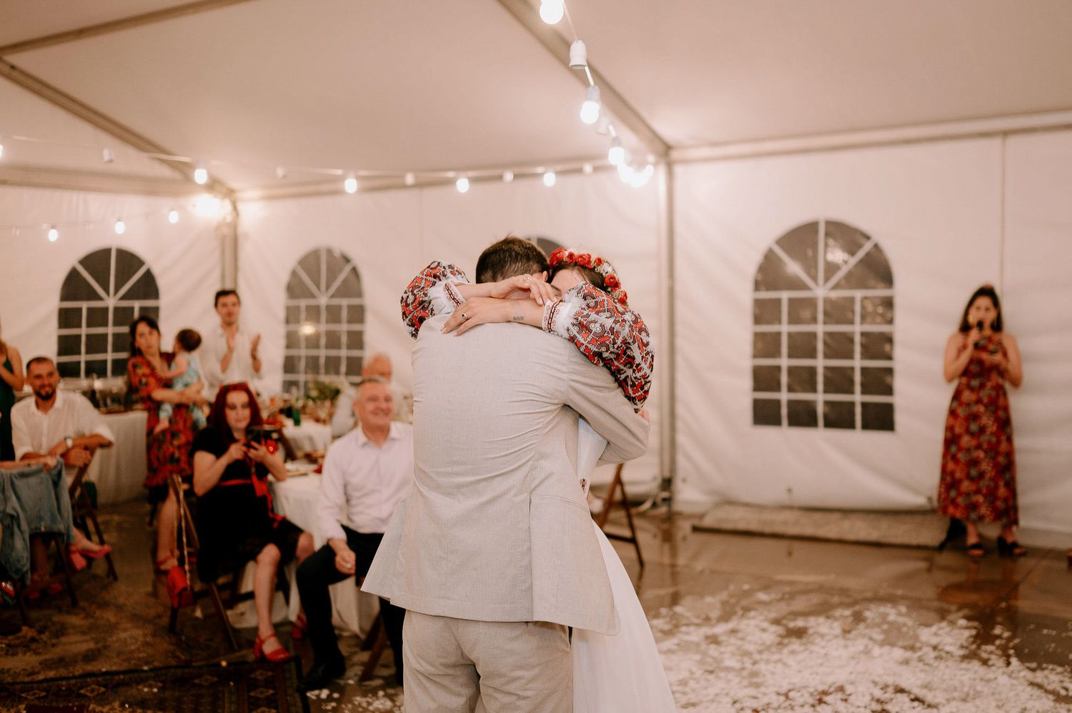 Wedding reception scene in a white tent with string lights and dancing guests.