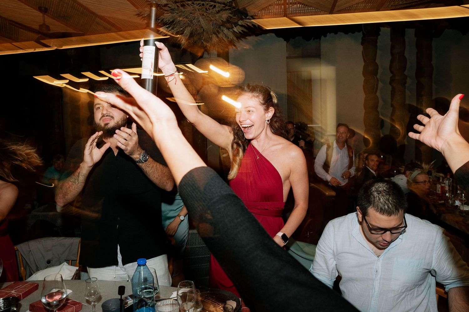 People celebrating and dancing with raised arms at a lively indoor party.