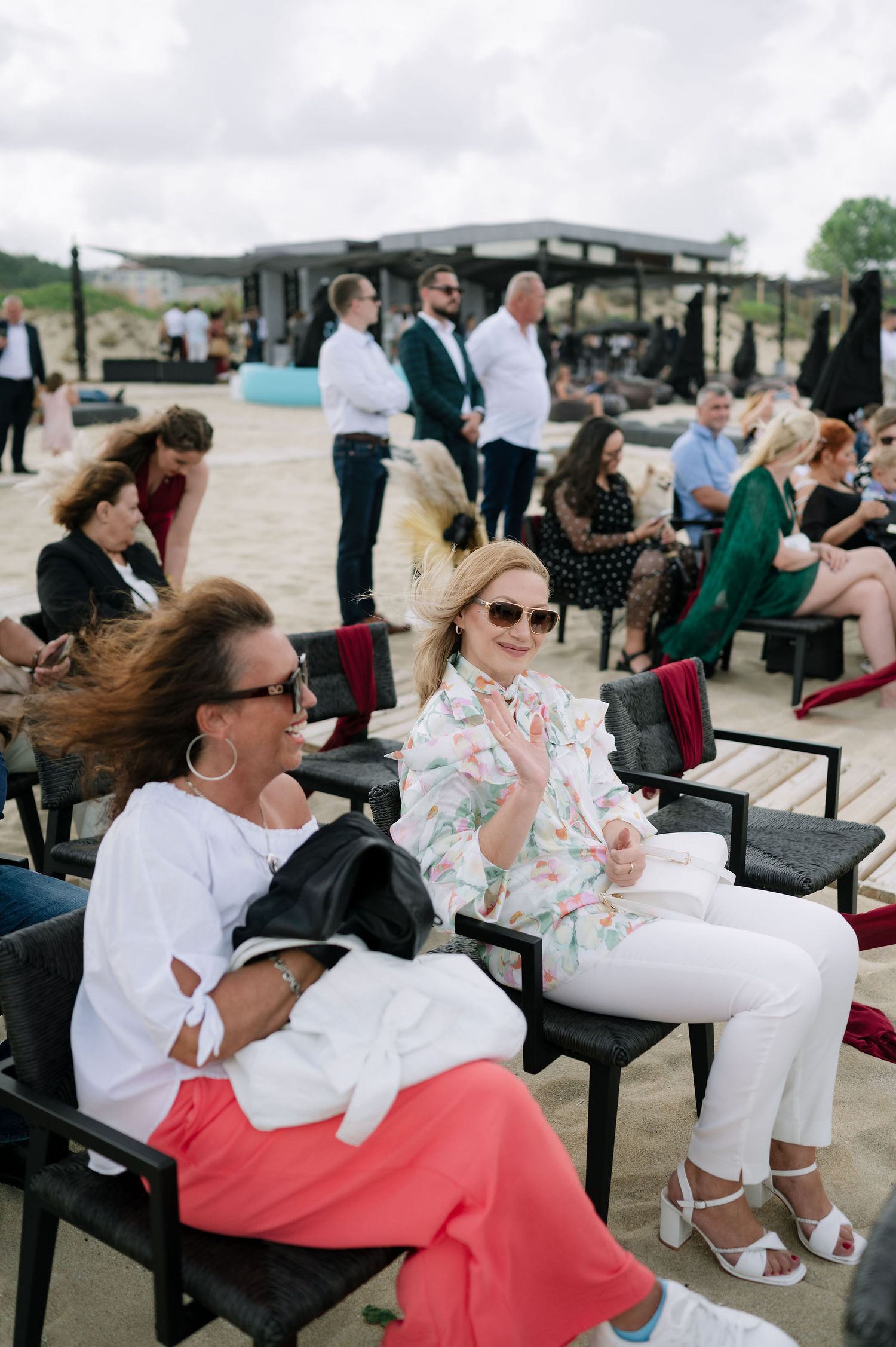Guests seated in modern black chairs at an outdoor seaside venue with windy conditions.