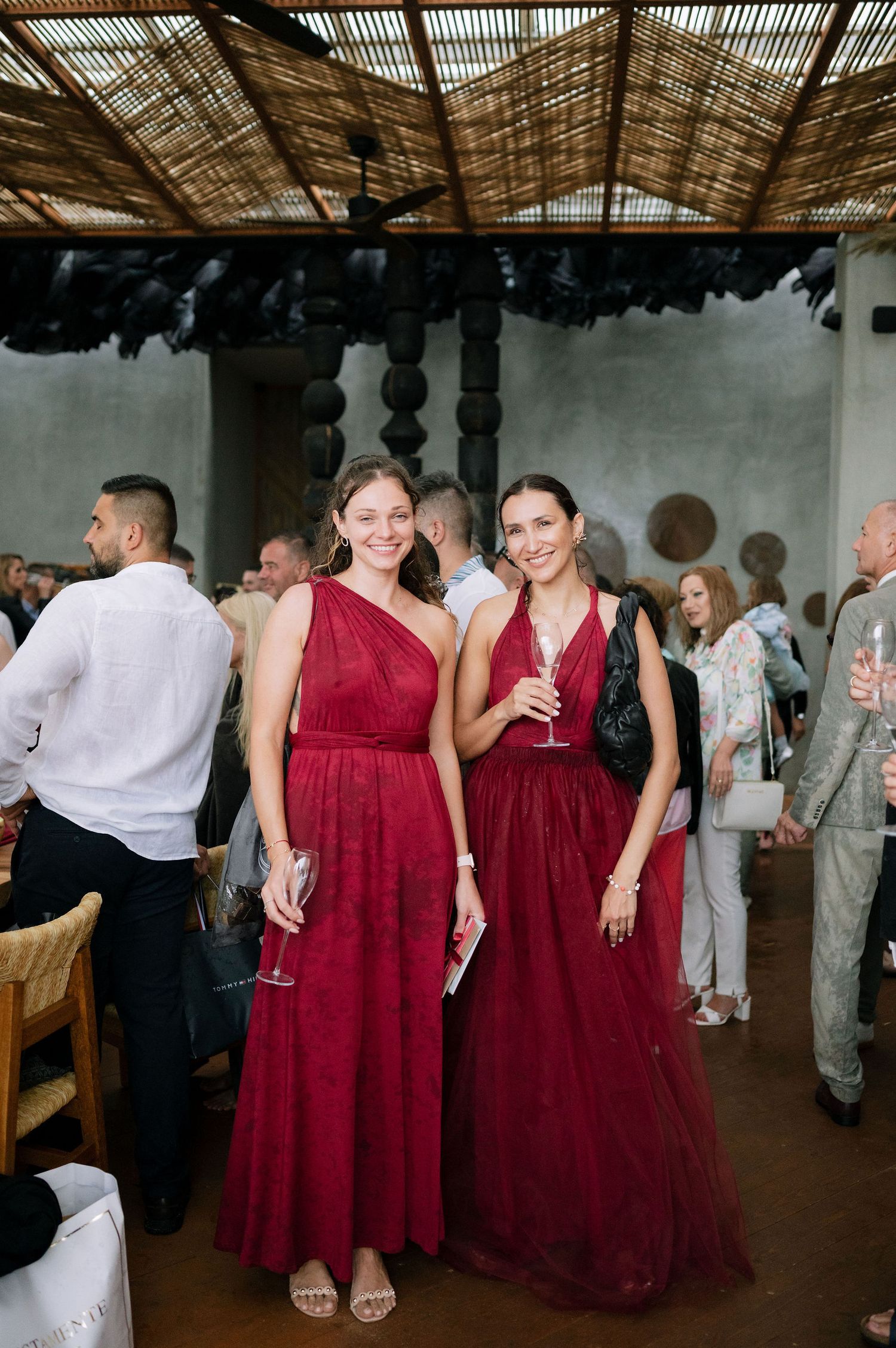Wedding guests in burgundy dresses and formal wear mingle under a rustic wooden ceiling.