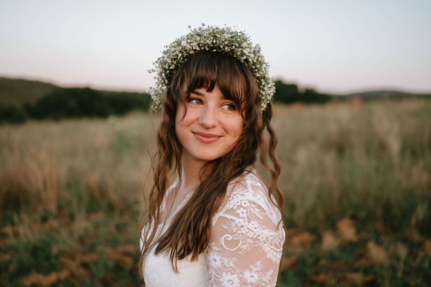 Bride with floral crown and lace gown poses against natural landscape backdrop.