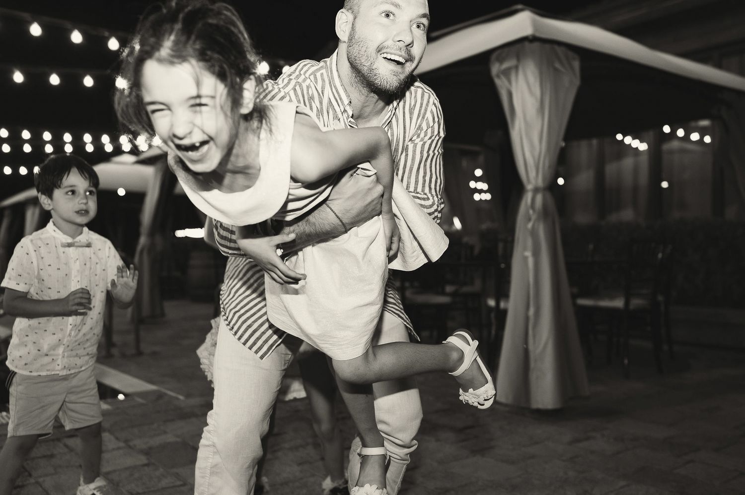 Black and white photo of playful piggyback ride at outdoor evening party.