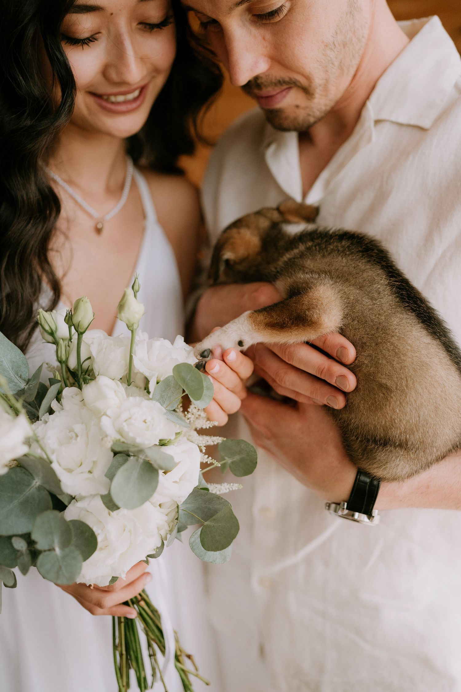 A romantic wedding photo series showing a couple embracing while holding a white floral bouquet with eucalyptus.