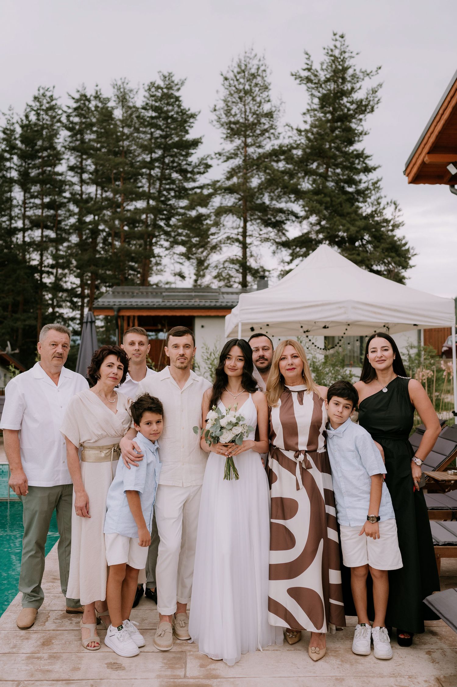 Wedding party in white attire gathered by a pool for a group photo.