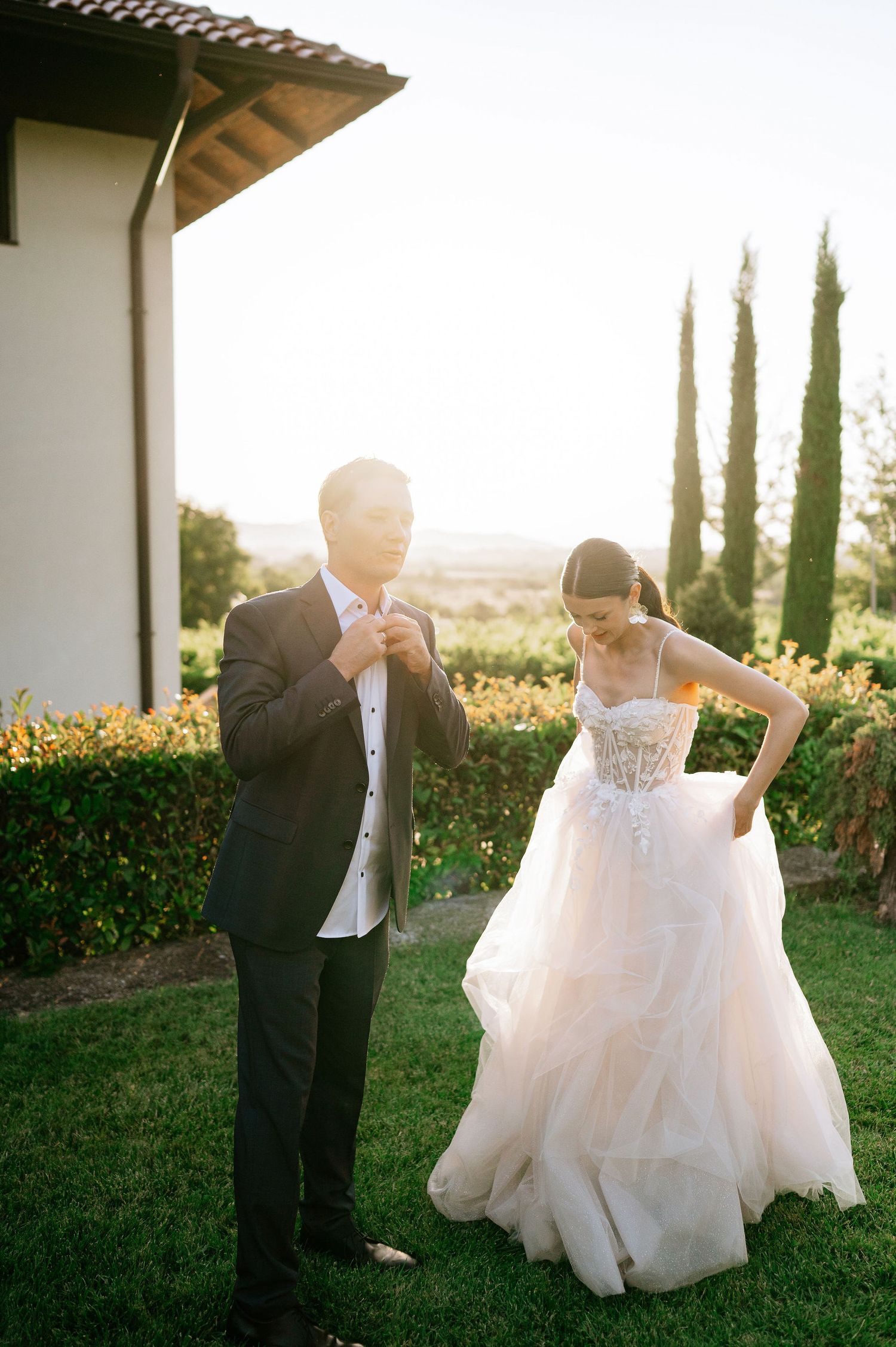 Couple dancing together on lawn with cypress trees and setting sun in background.