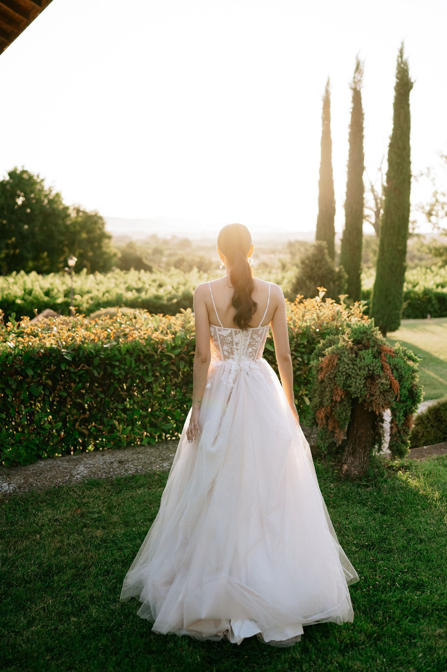 Elegant bridal gown with detailed lace bodice and tulle skirt photographed in a garden at sunset.