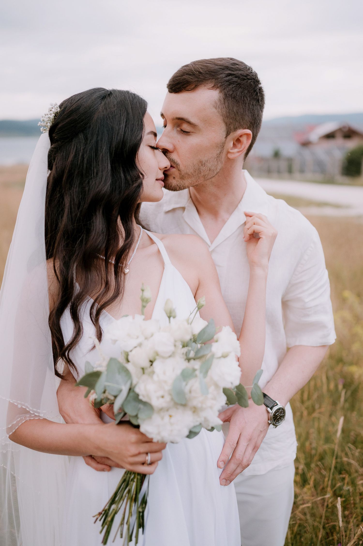 A couple in white wedding attire shares intimate moments in a rustic field setting.