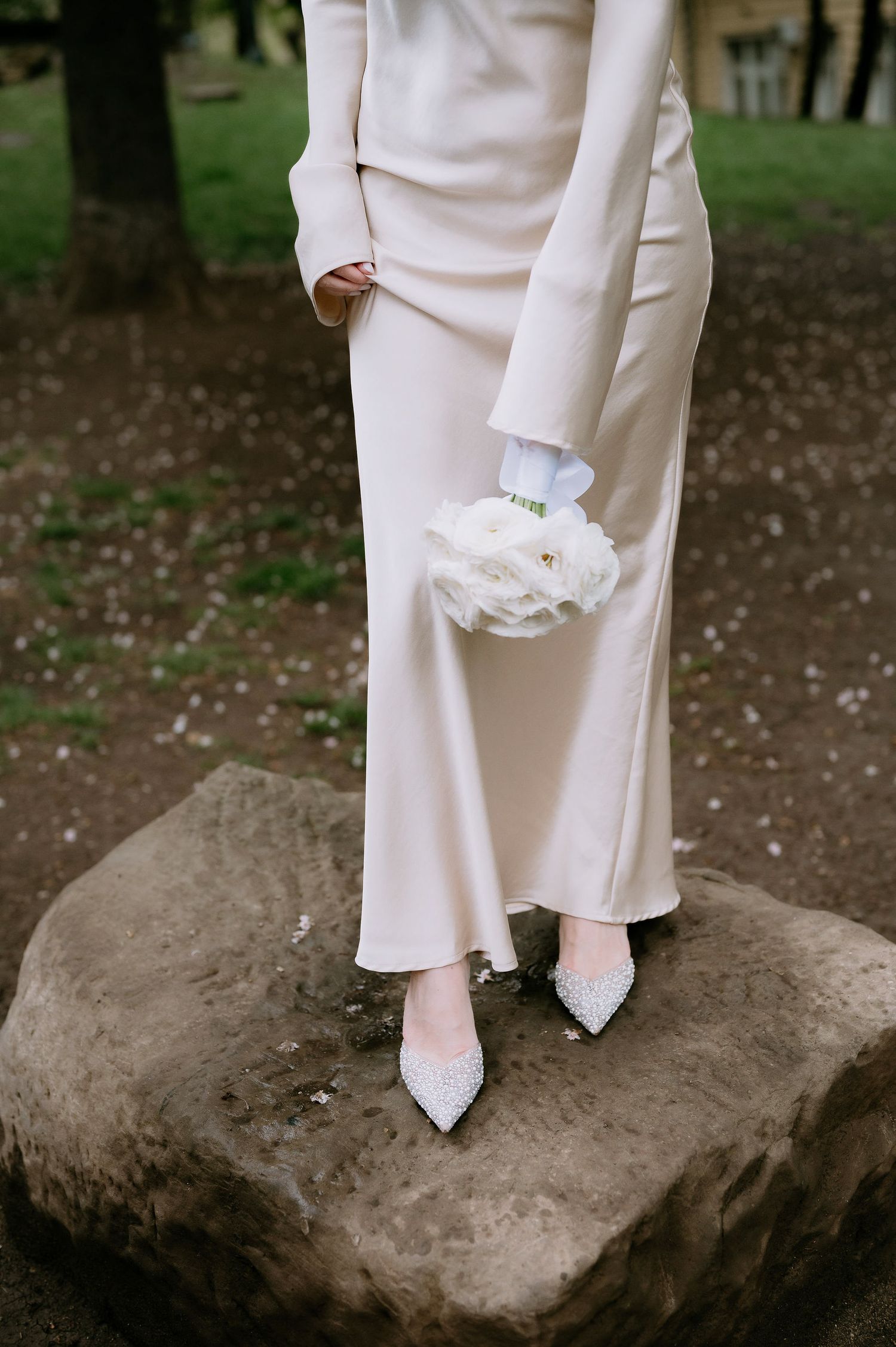 White wedding shoes and dress hem photographed on natural stone in an outdoor setting.