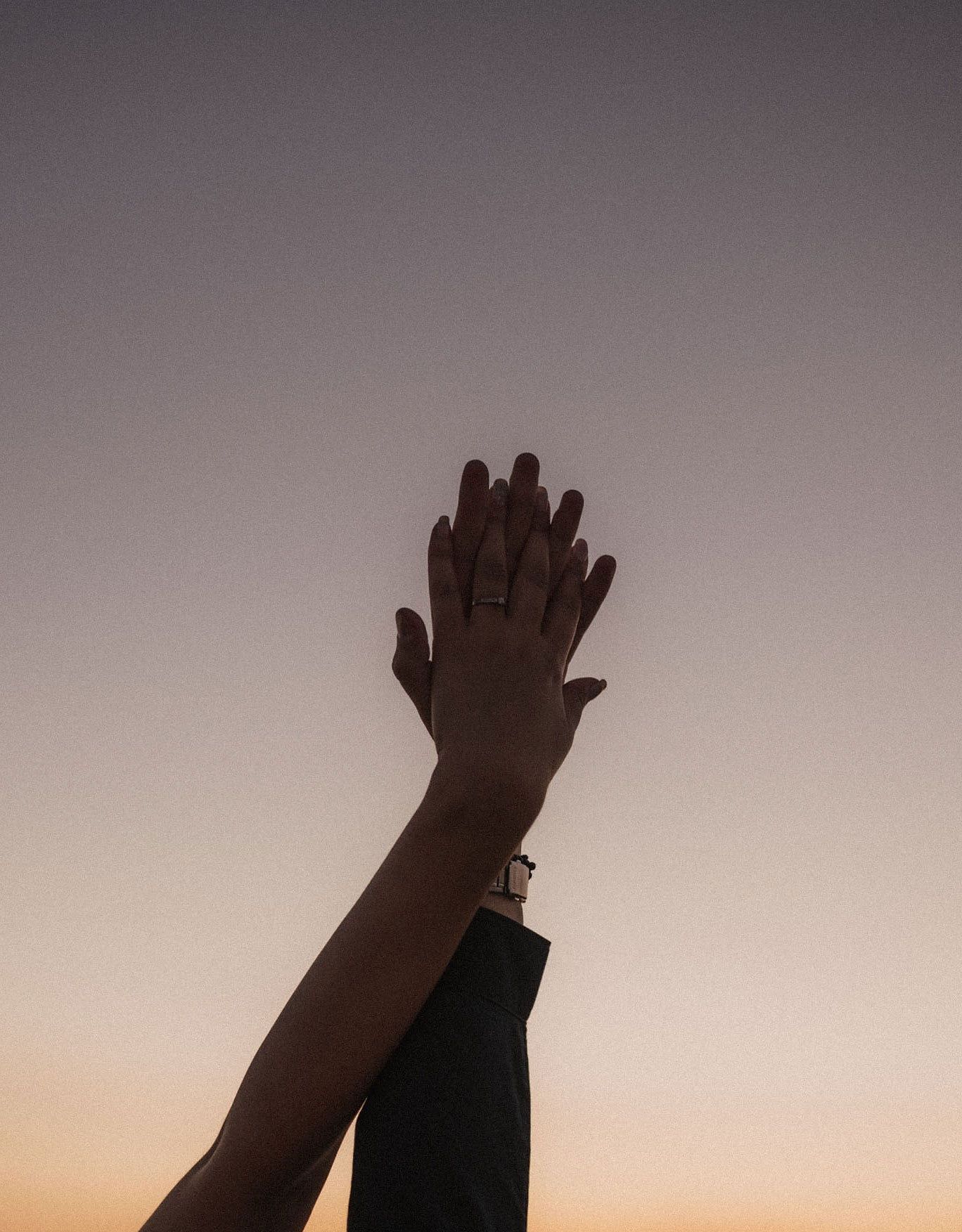Silhouetted hands raised against a dusky gradient sky.