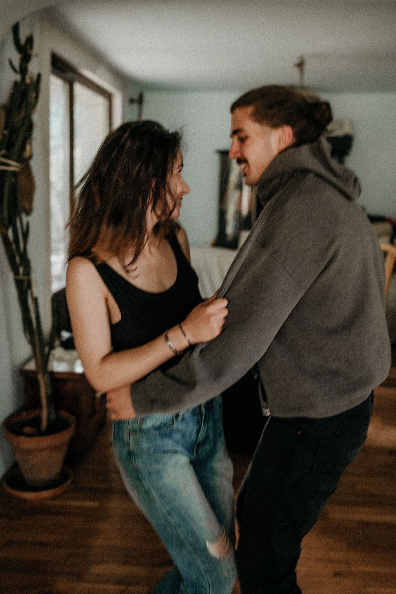 A couple shares joyful dancing moments together in their home with natural window lighting.
