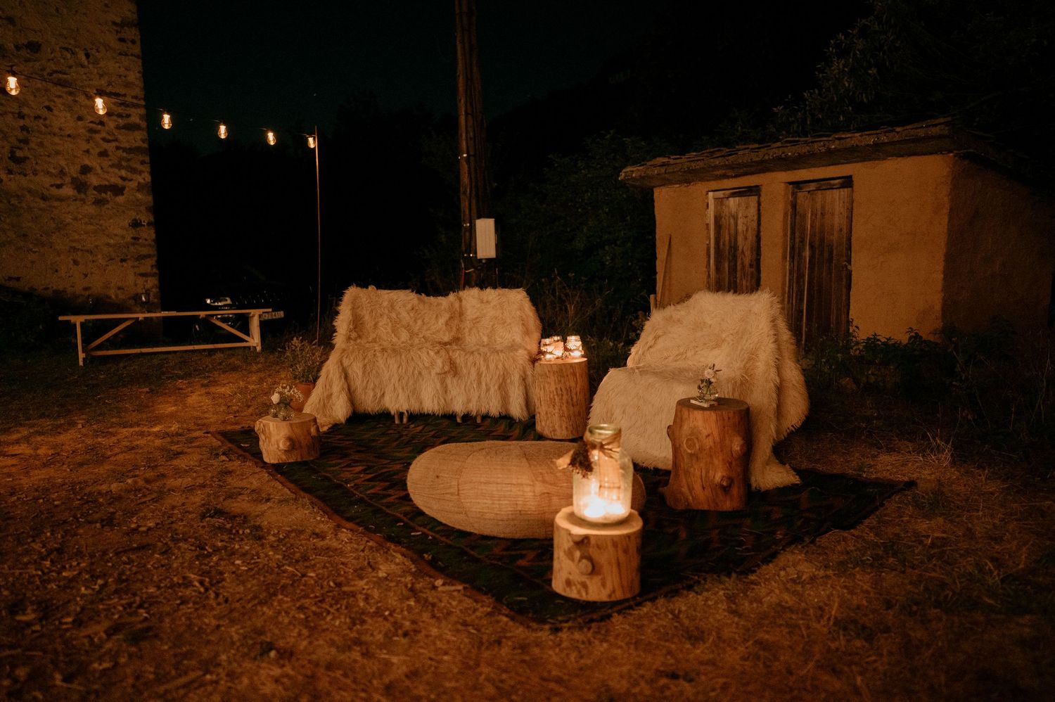 Rustic outdoor venue at night illuminated by warm string lights and lanterns.